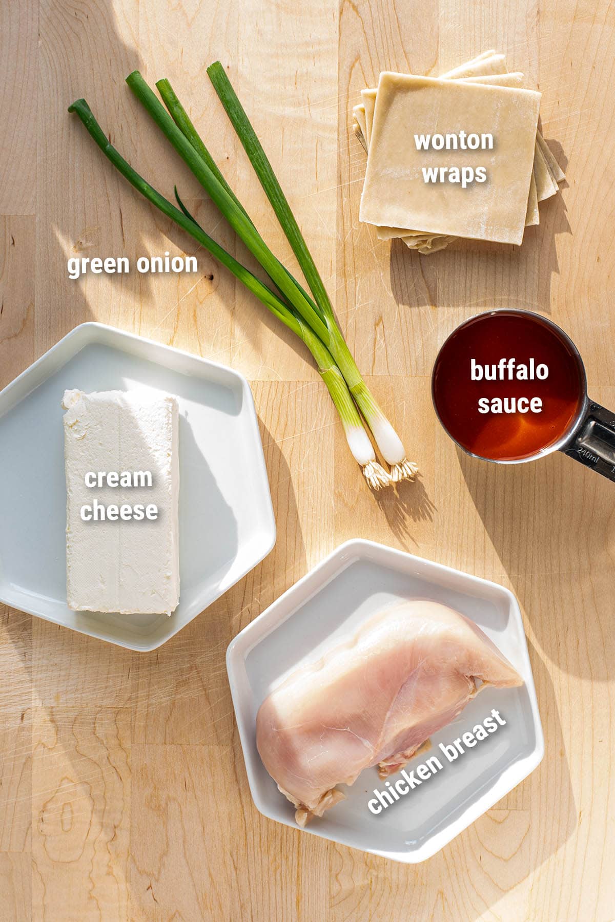 Raw, uncooked ingredients for buffalo chicken rangoons lais out on a wooden cutting board.