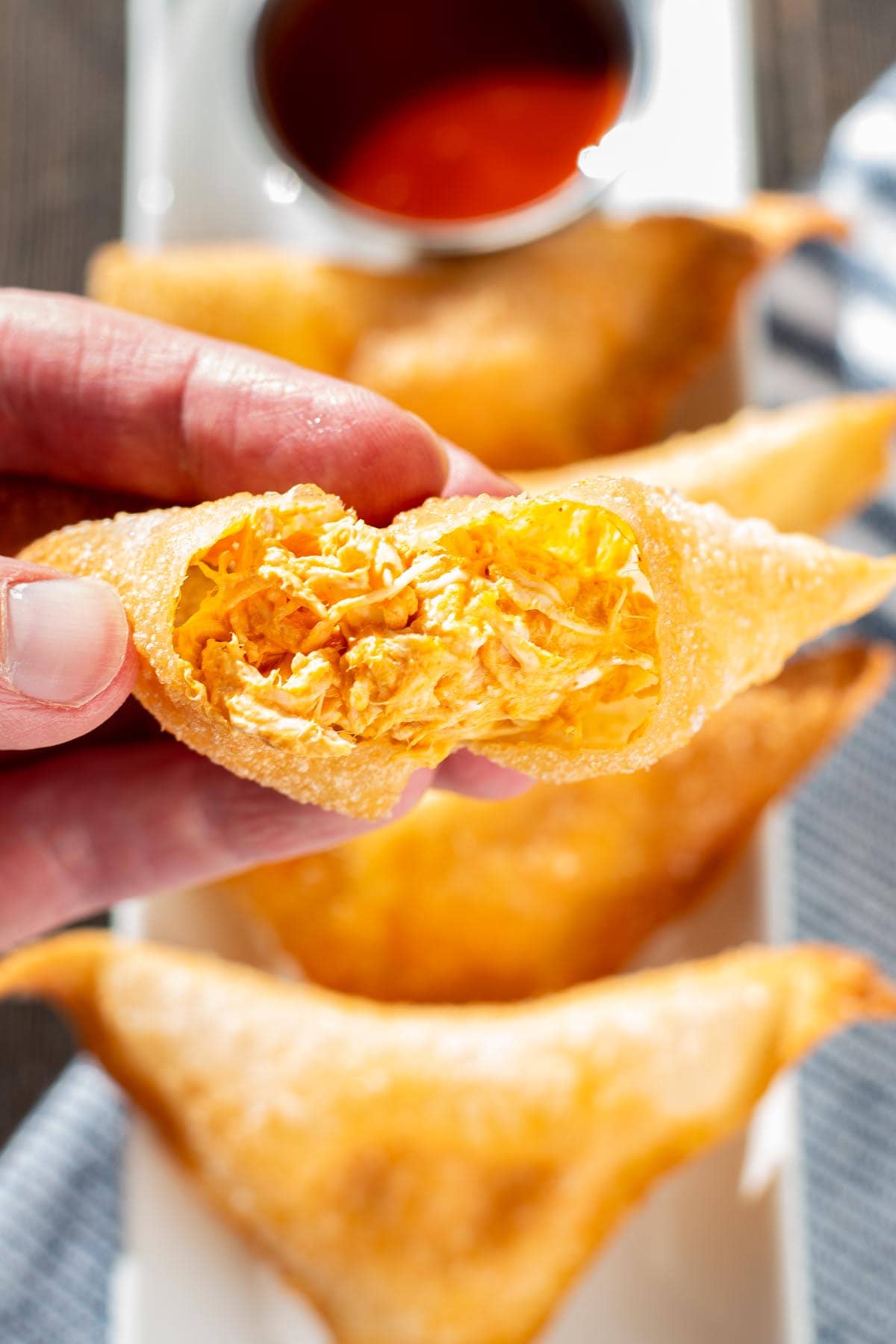 A hand breaking open a golden fried buffalo chicken rangoon to reveal the creamy cheesy orange buffalo filling.
