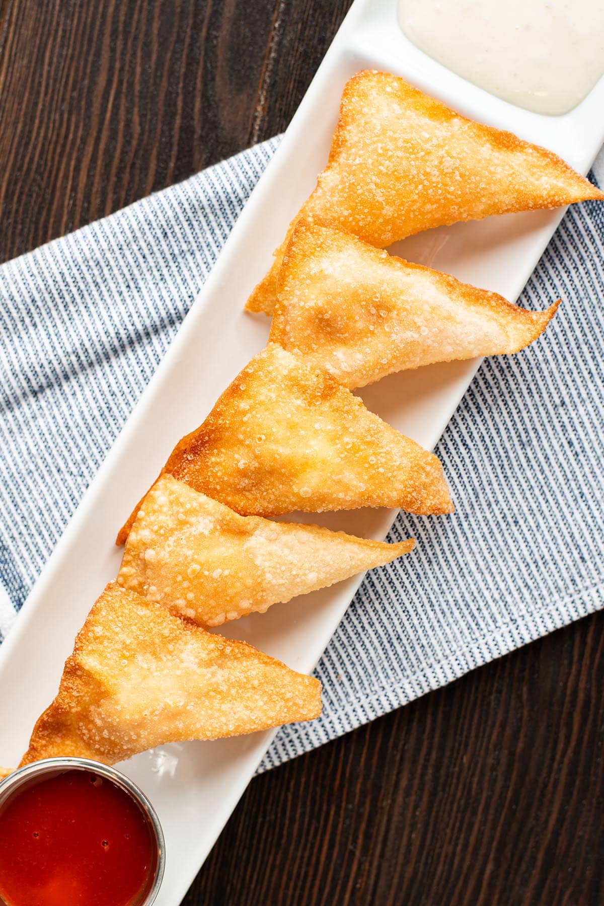 Five Fried buffalo chicken rangoons on a slender white serving platter served with buffalo sauce and blue cheese dressing.