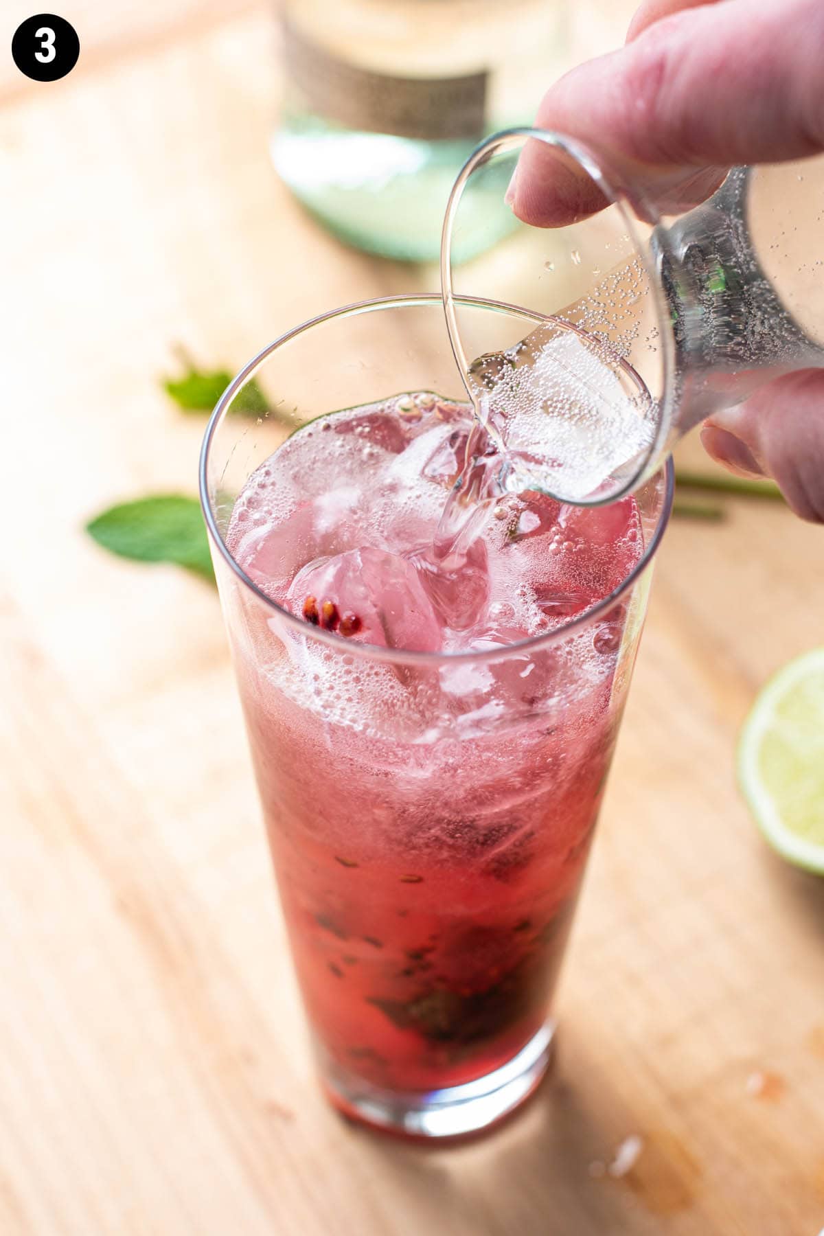 A handy pouring fizzy club soda on top of a blackberry mojito cocktail.