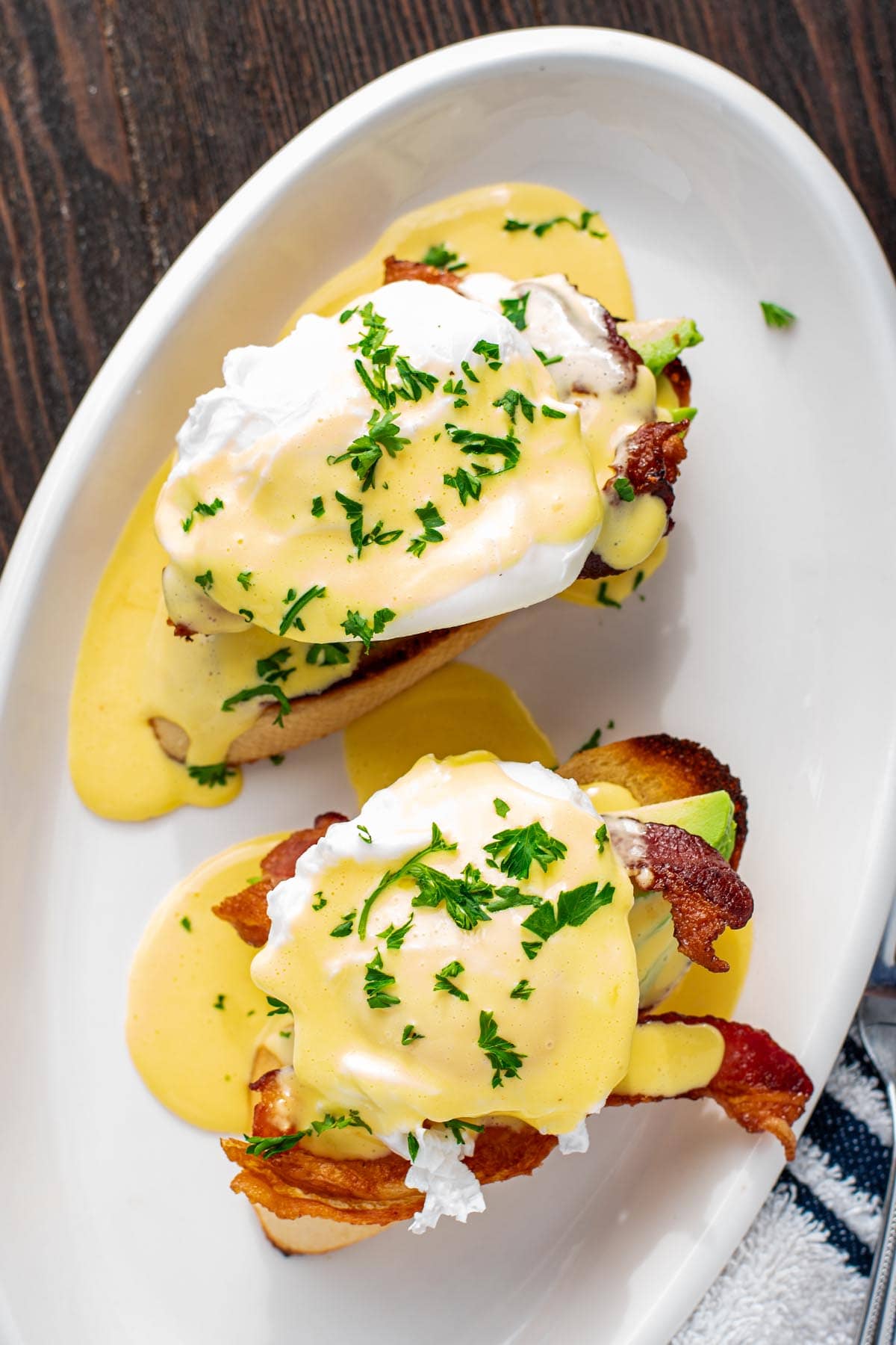 Eggs benedict made with bacon and sliced avocado on top of golden toasted French bread.