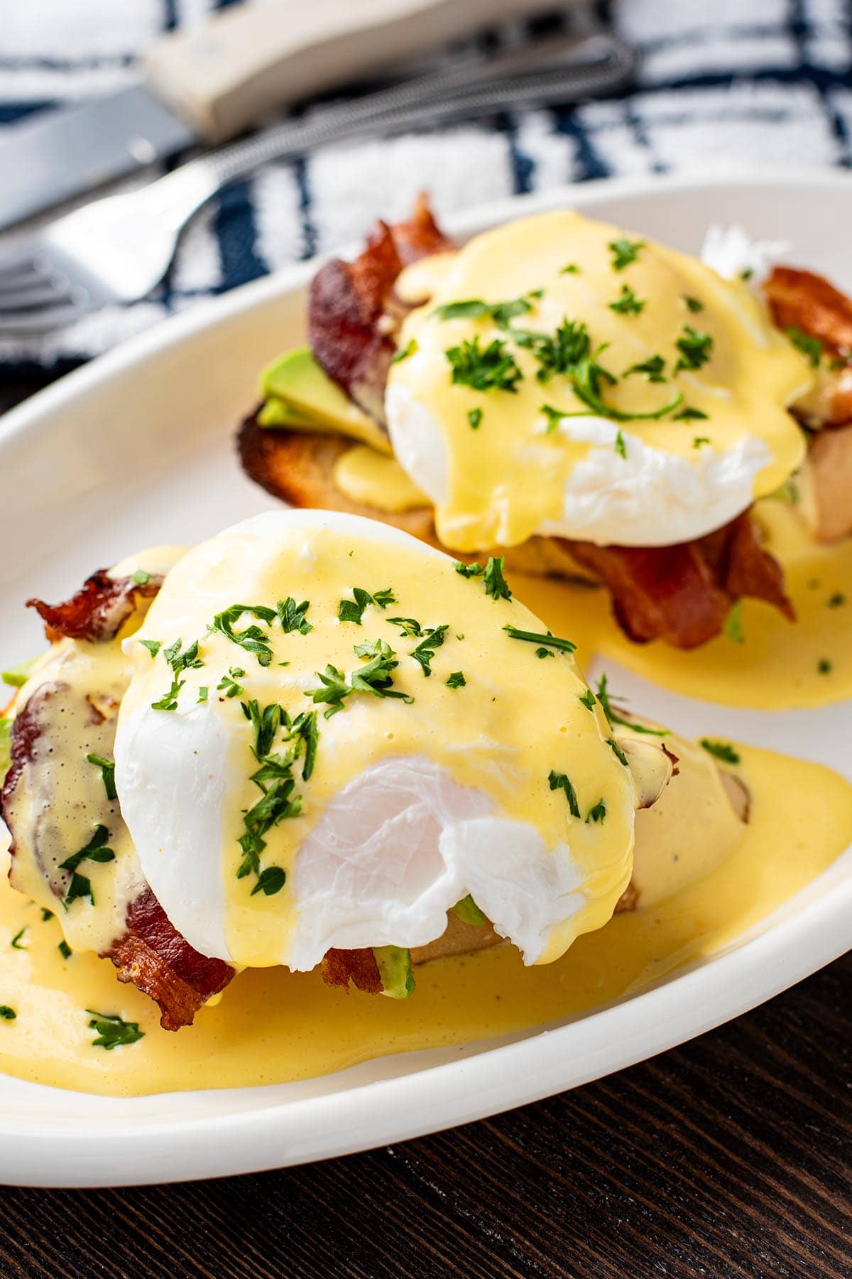 Eggs benedict made with bacon and sliced avocado on top of golden toasted French bread.