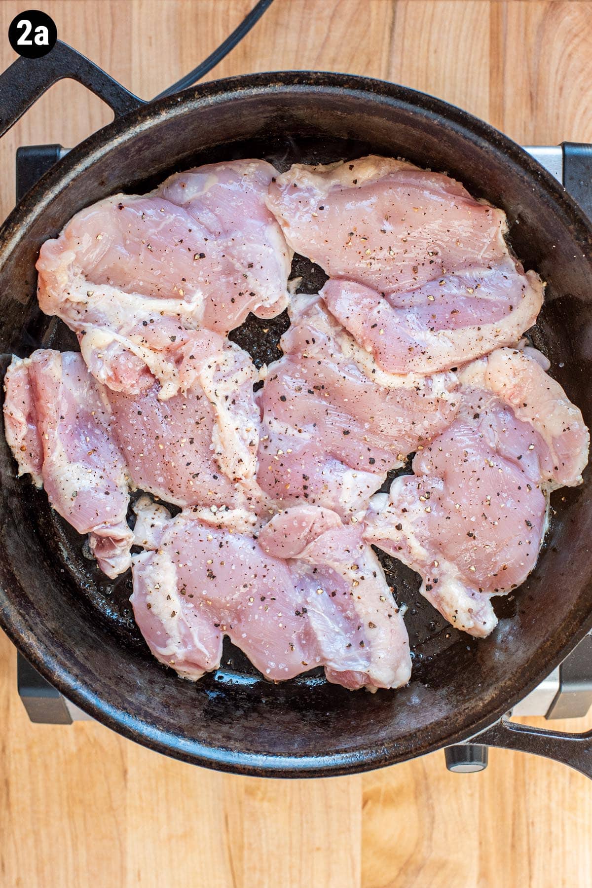 Uncooked, seasoned boneless chicken thighs pan searing in a cast iron skillet.