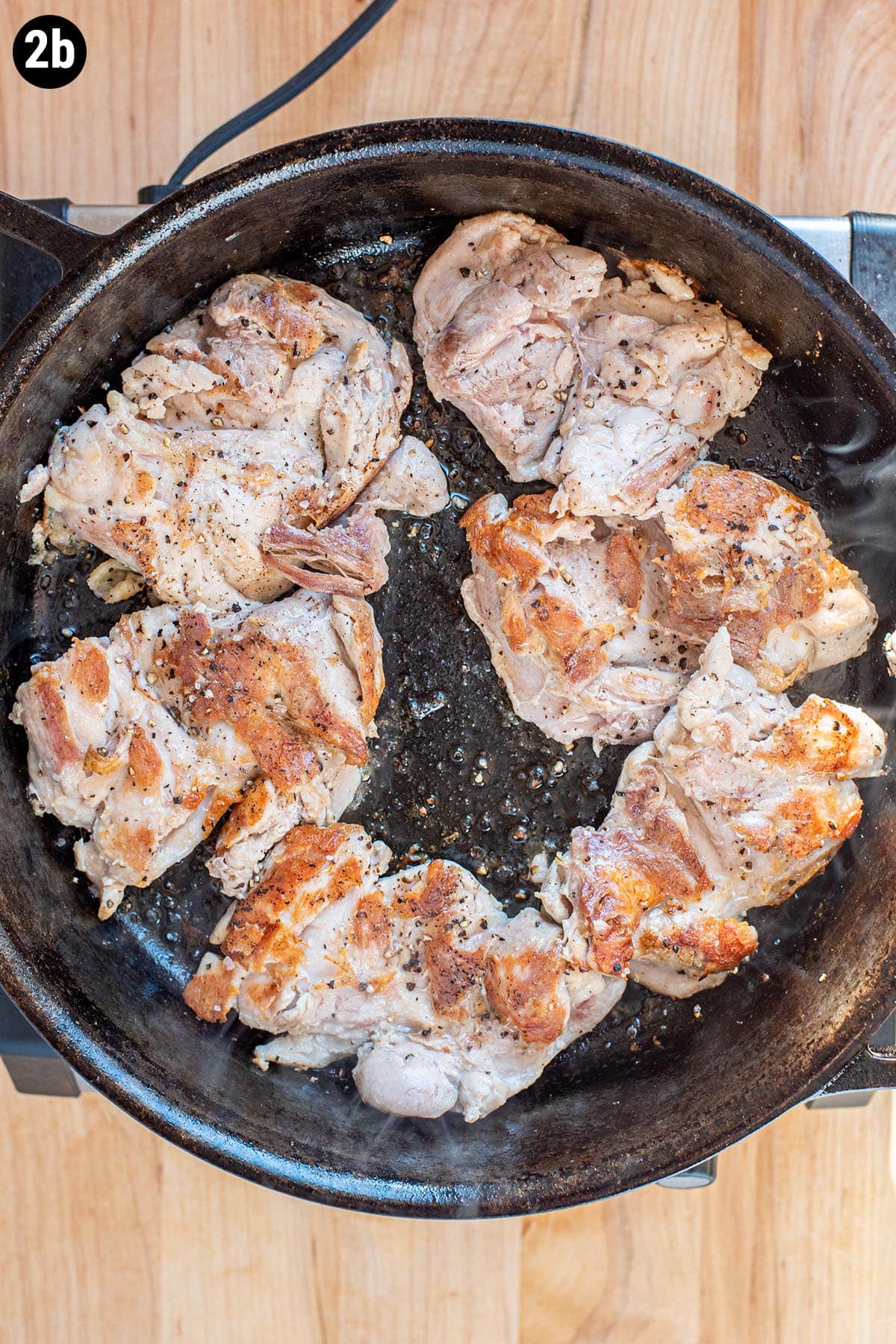 Browned, pan seared chicken thighs cooking in a cast iron skillet.