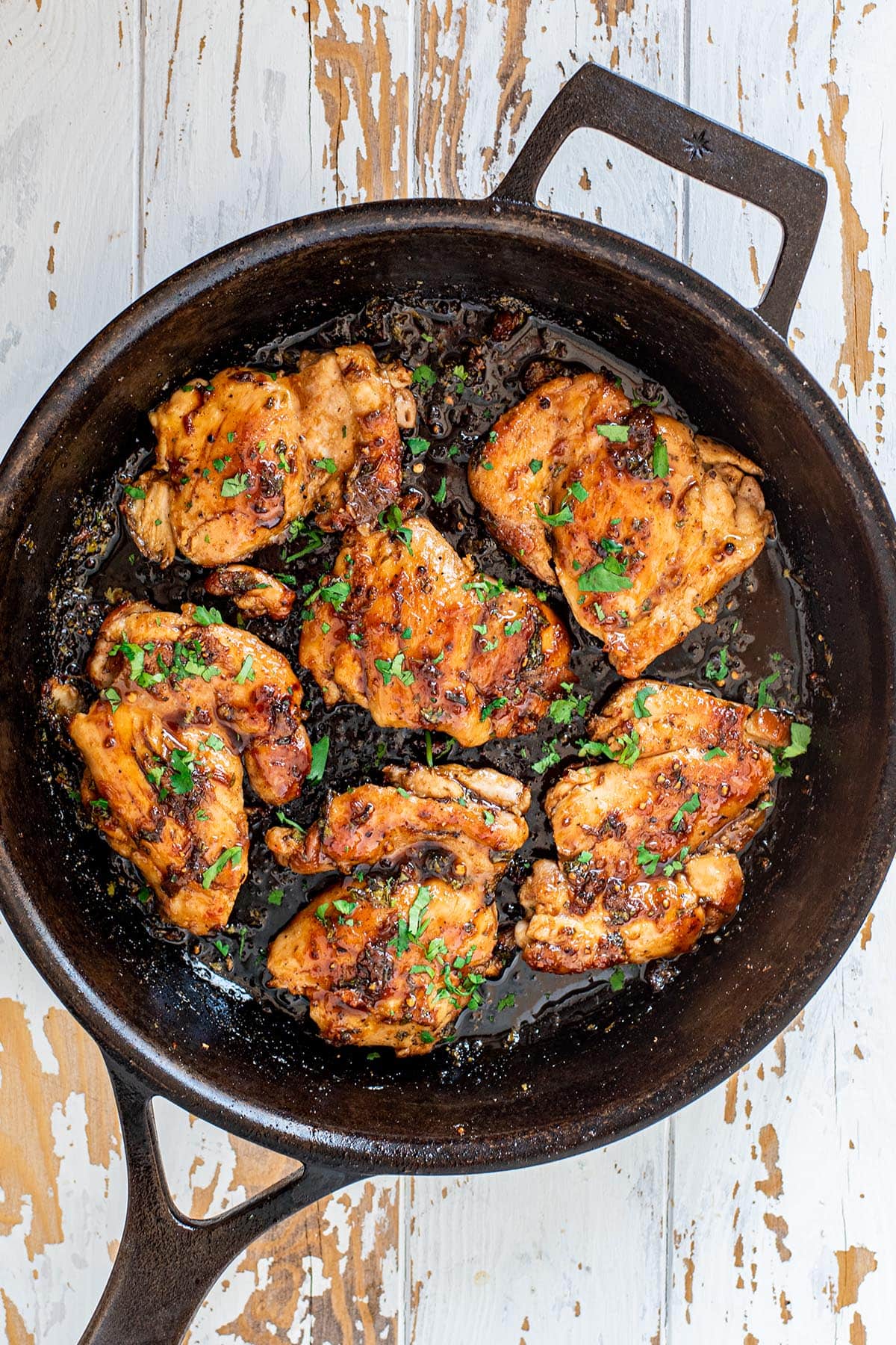 Golden cilantro lime chicken covered in a sticky glaze and fresh cilantro in a cast iron skillet.