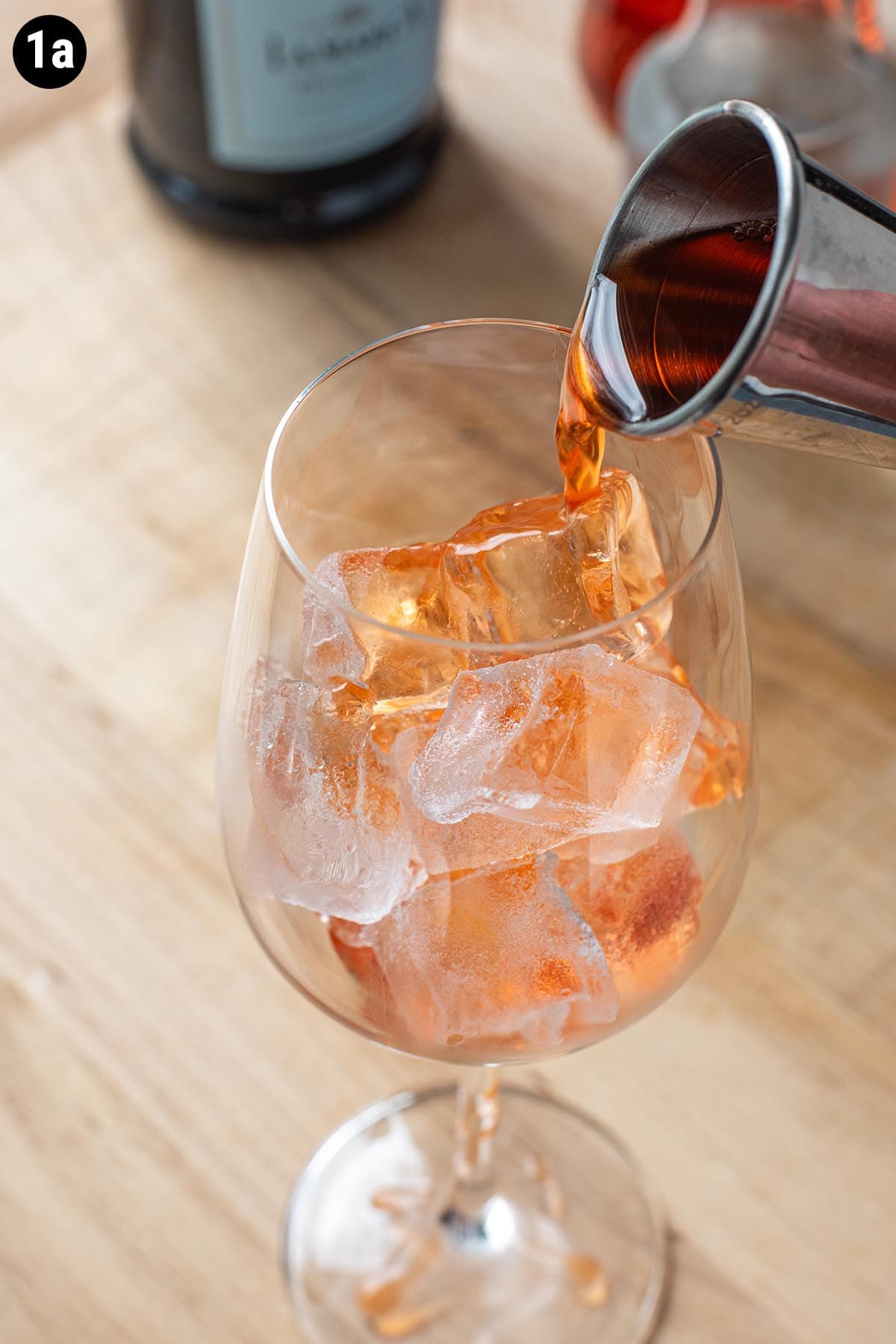 Pouring Aperol into a wine glass full of ice with a double jigger.