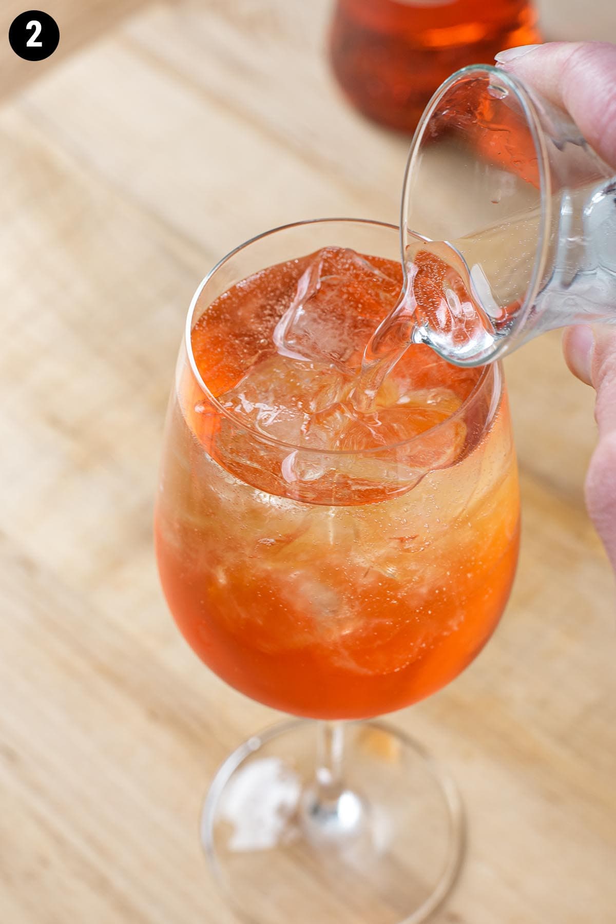 Pouring sparkling water into an Aperol Spritz.