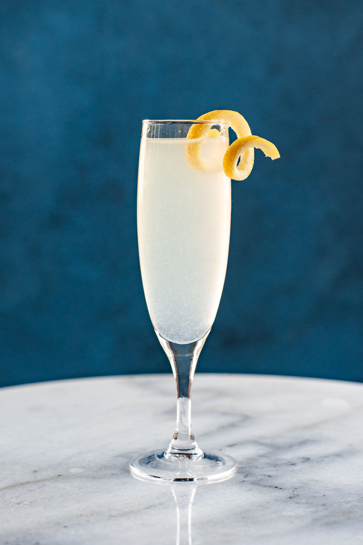 A French 75 cocktail garnished with a lemon twist on a white marble table.