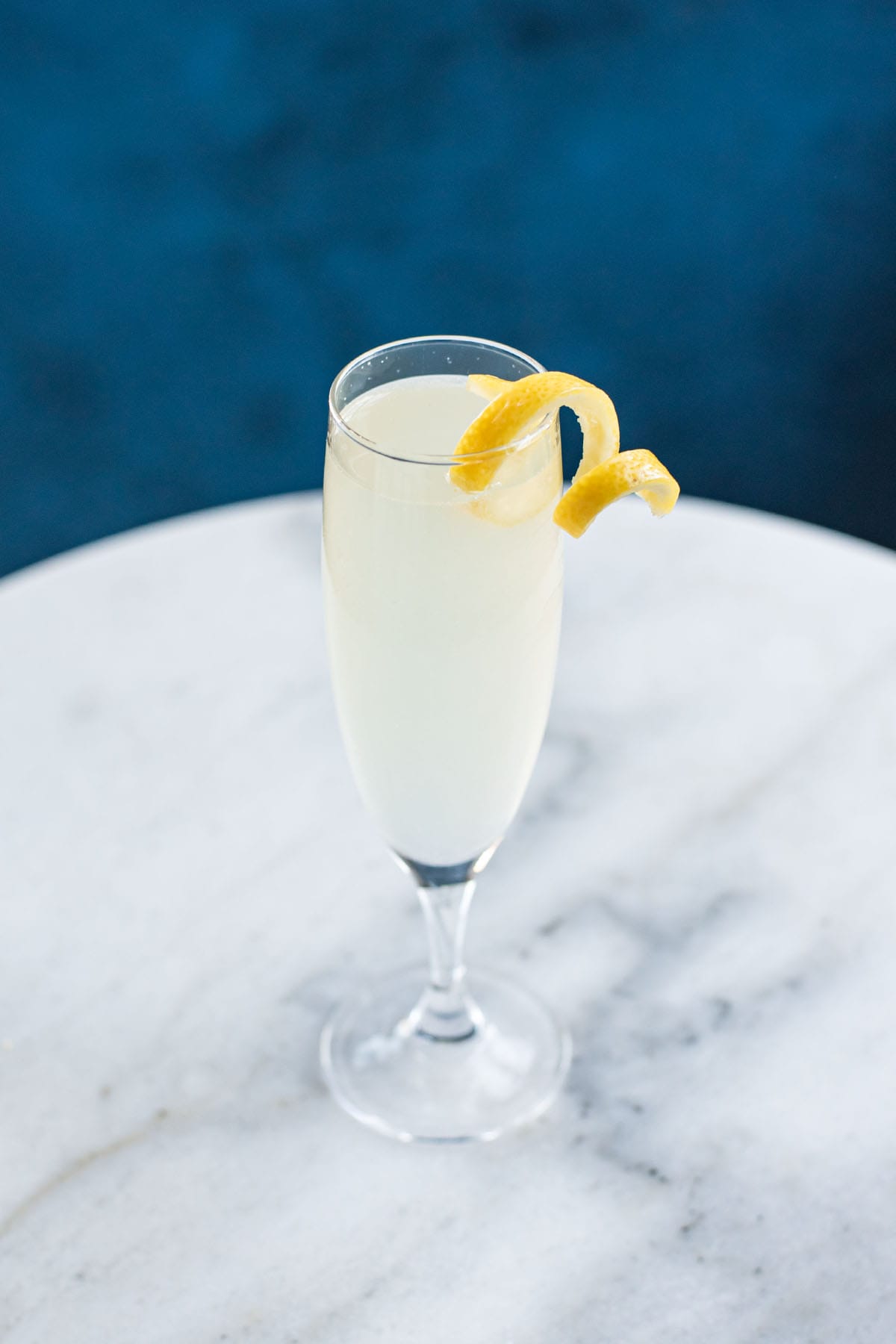 A French 75 cocktail garnished with a lemon twist on a white marble table.