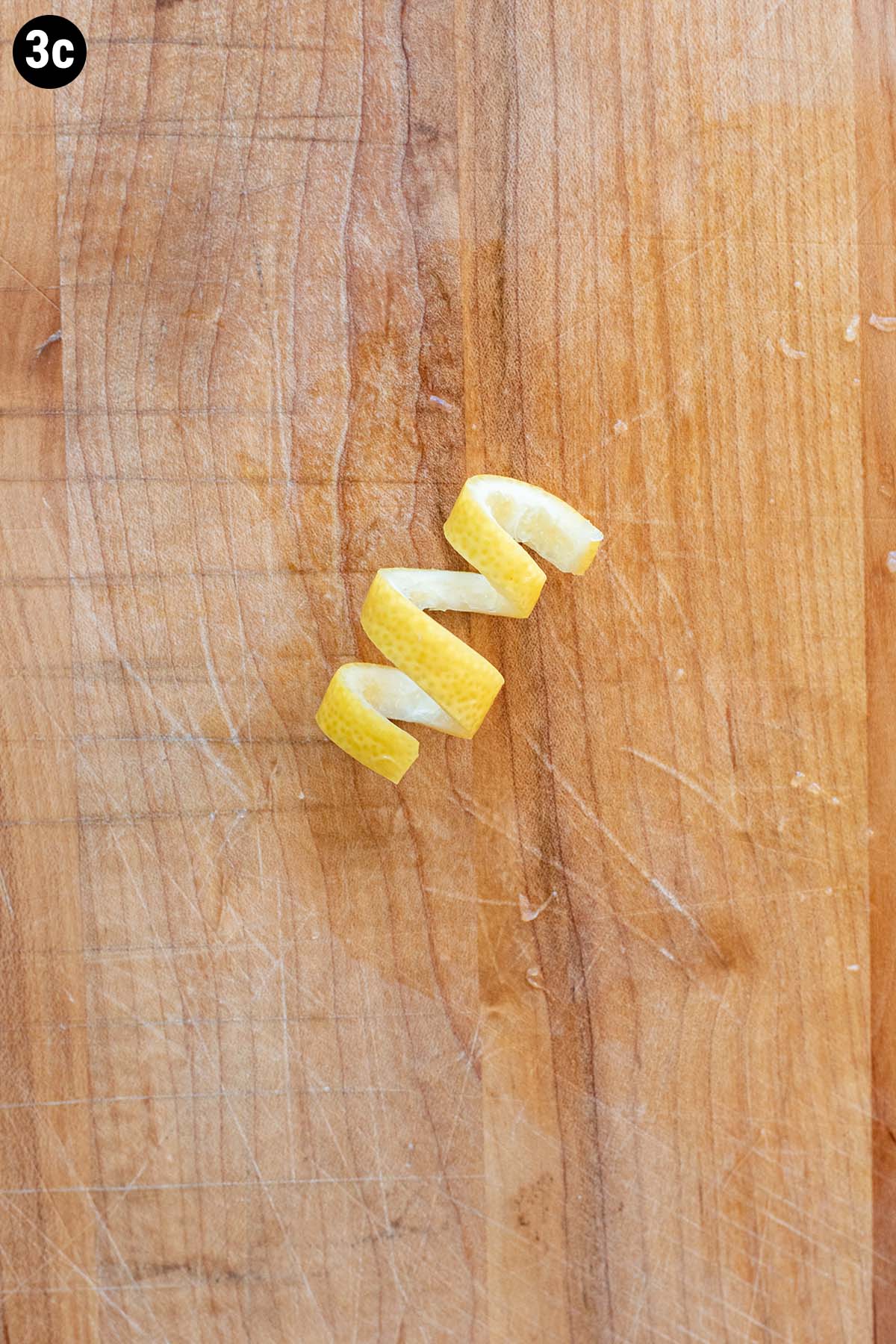 A lemon twist on a wooden cutting board.