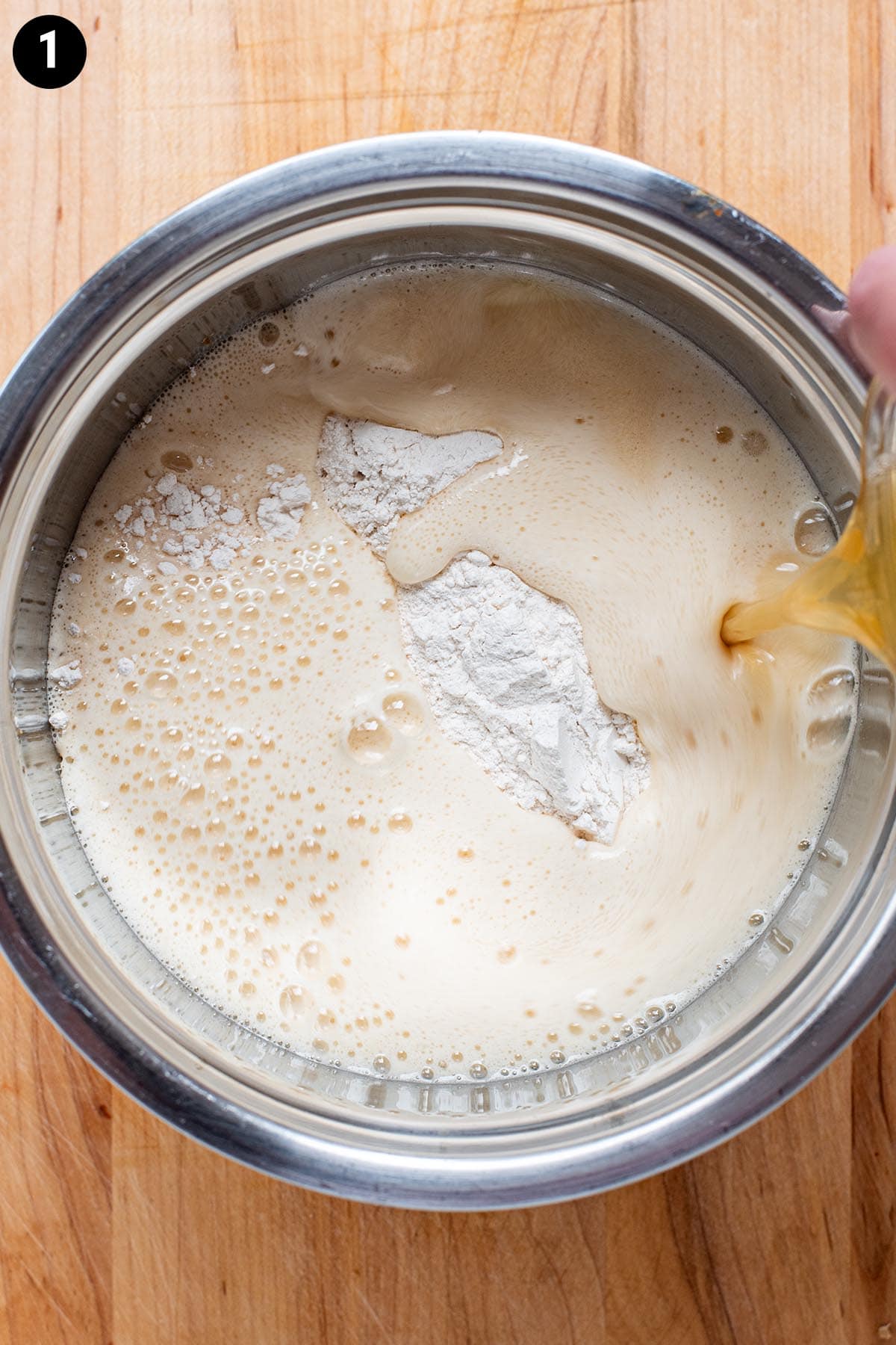 Pouring beer into flour in a stainless steel bowl for beer batter.