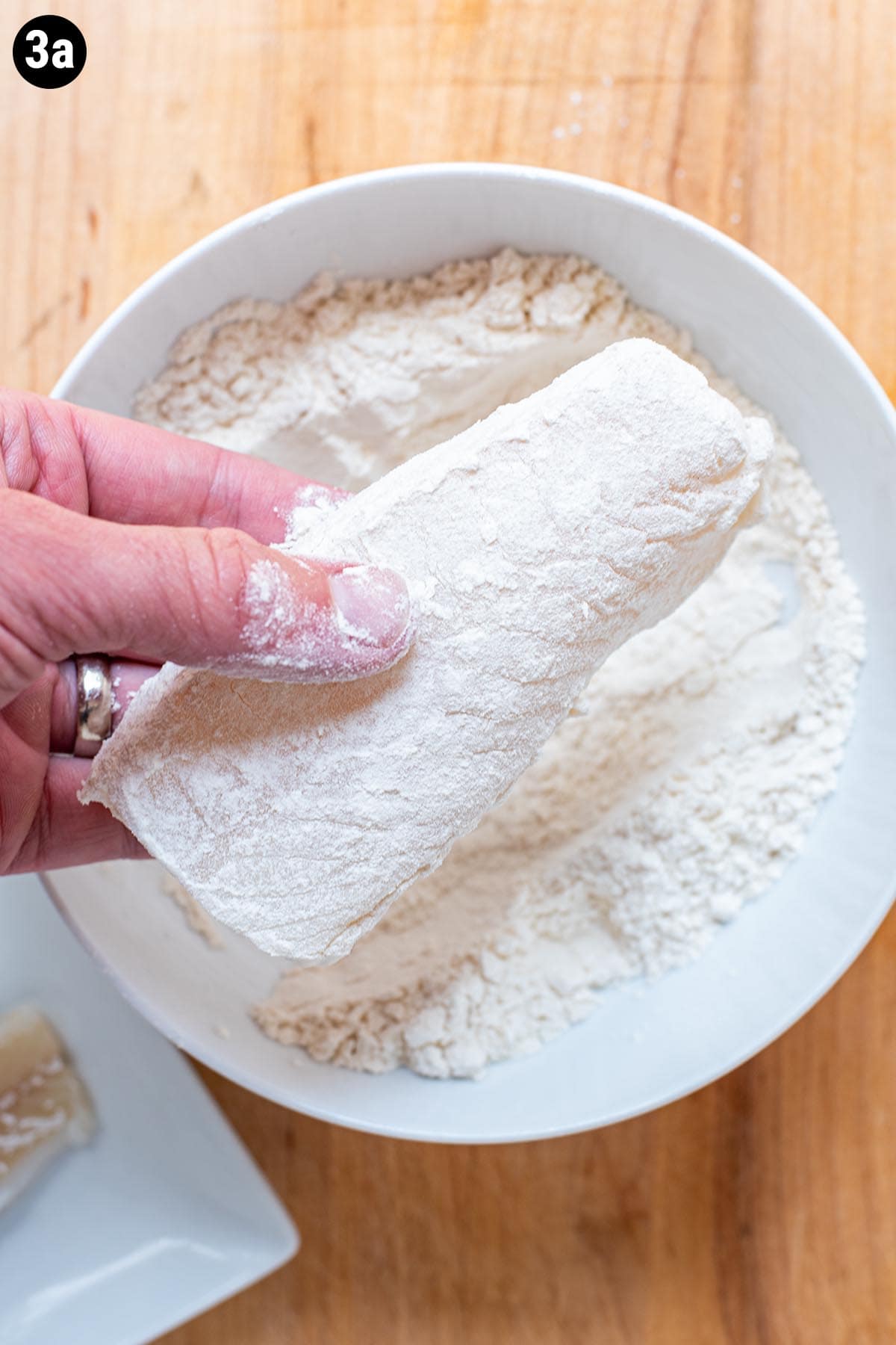 Dredging a piece of raw cod in flour.
