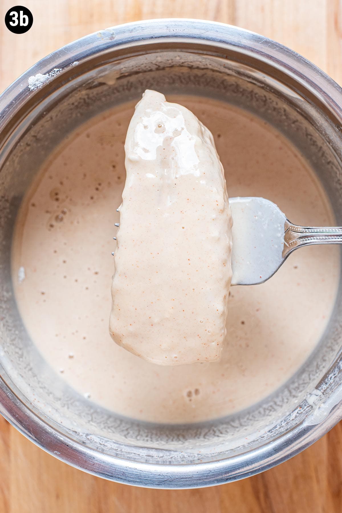 A fork holding a piece of cod after it has been dopped in beer batter.