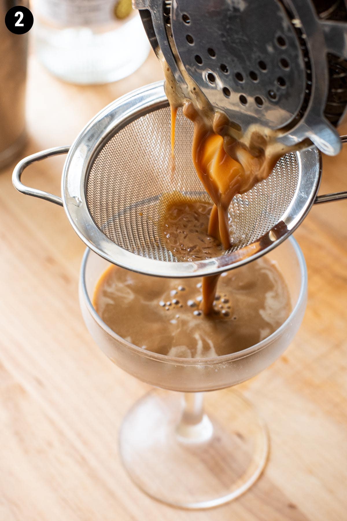 Double straining a chocolate espresso martini into a chilled coupe glass.