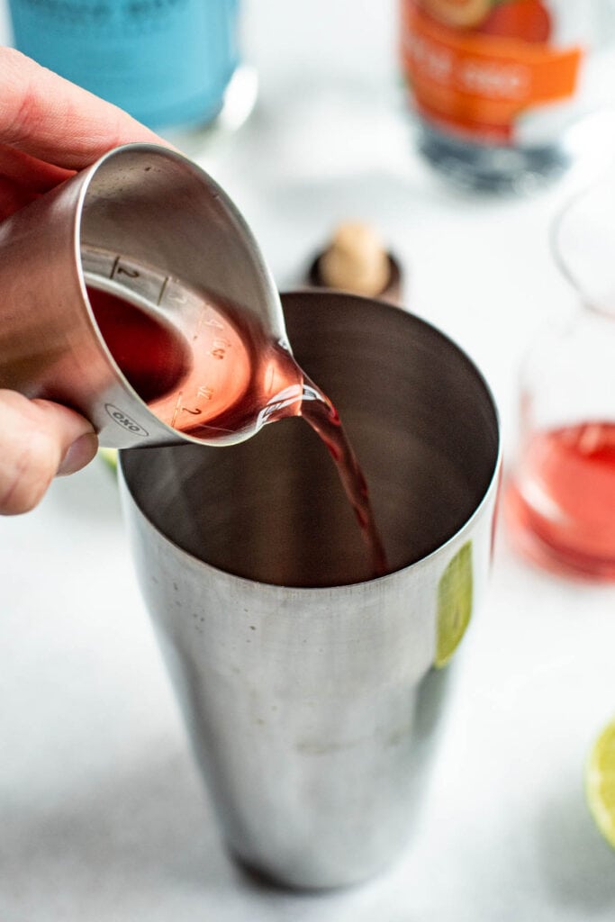 Pouring cranberry juice into a cocktail shaker with a jigger.