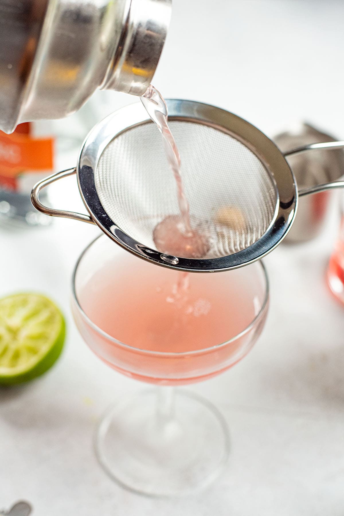 Double straining a Cosmopolitan cocktail into a chilled coupe glass.