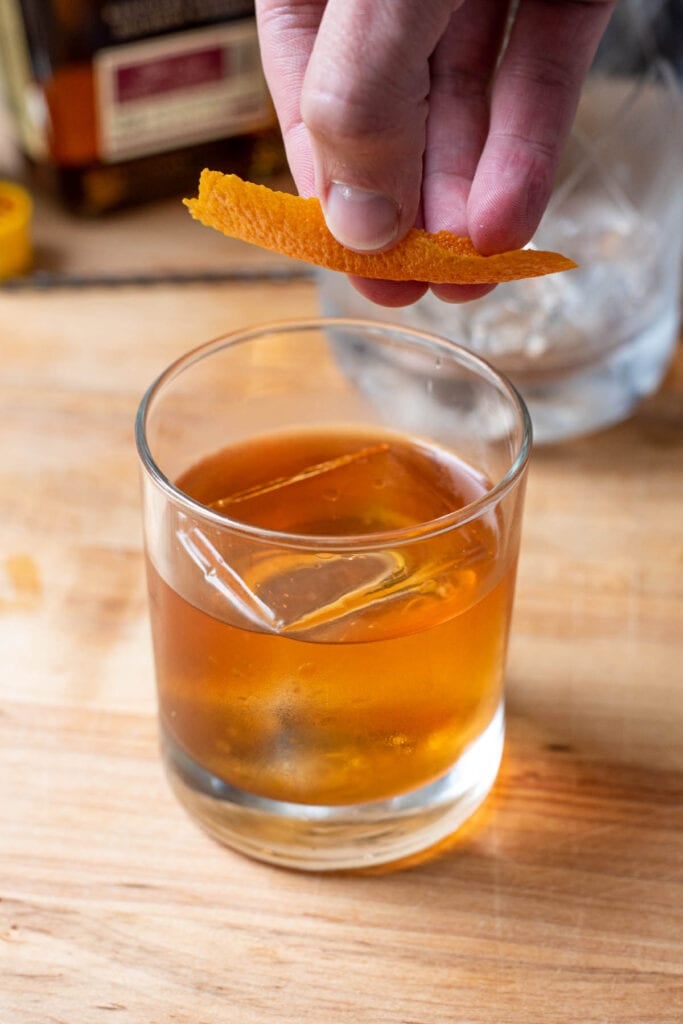 Expressing an orange peel over a whiskey cocktail with a clear ice cube.