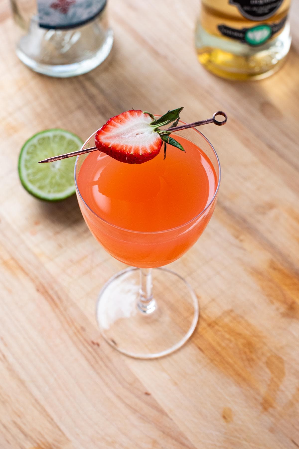 A red strawberry martini garnished with a sliced strawberry served in a Nick and Nora Glass.