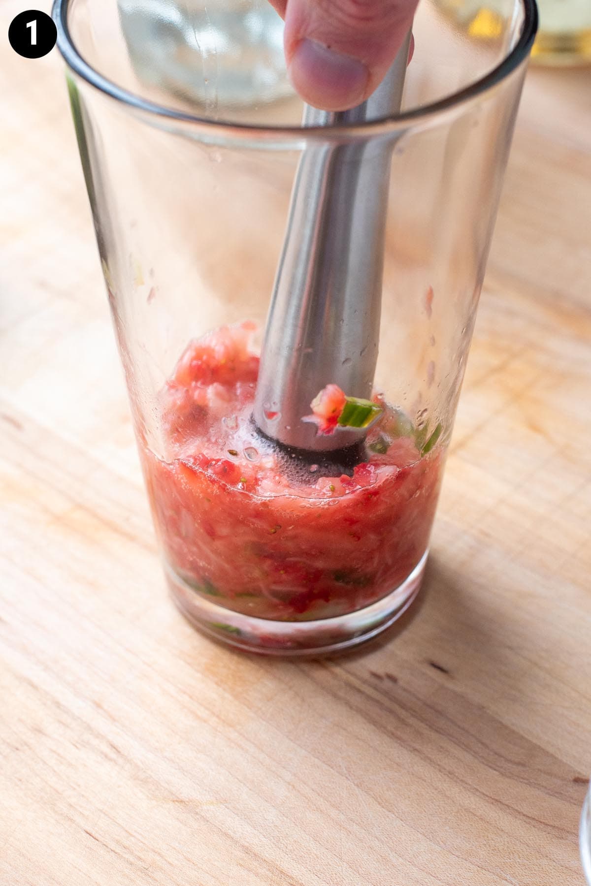 Muddling strawberries and sliced cucumbers together in a pint glass with a stainless steel muddler.