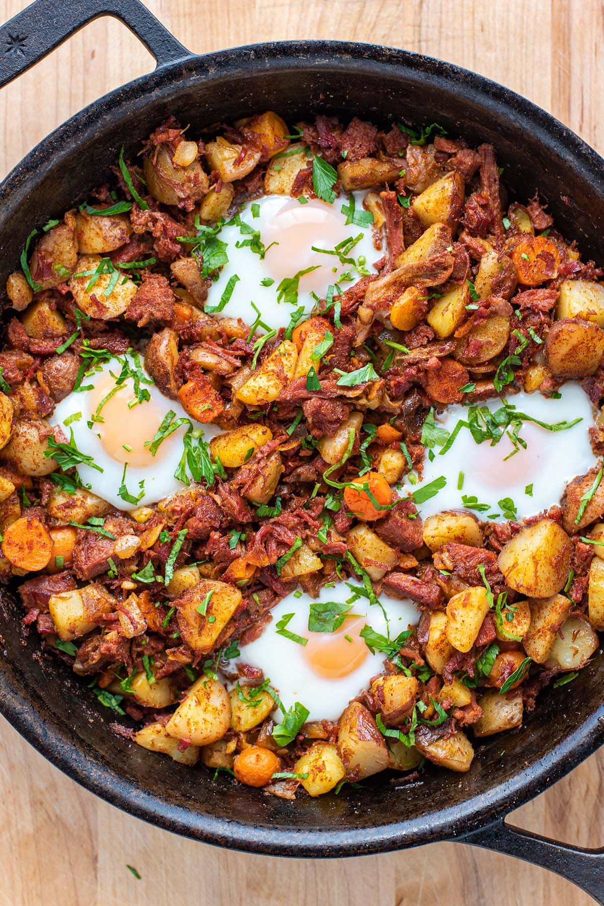 Golden corned beef breakfast hash topped with baked runny eggs and fresh parsley.
