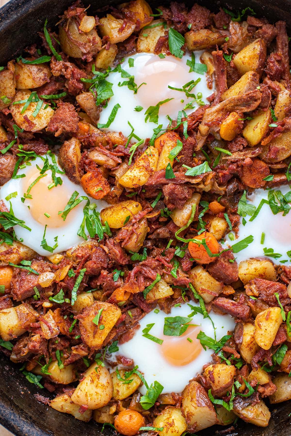 Golden corned beef breakfast hash topped with baked runny eggs and fresh parsley.