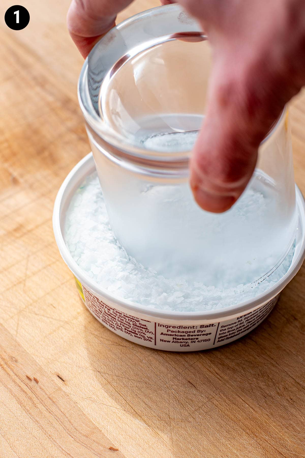 Dipping a chilled double old fashioned glass in a container of margarita salt.