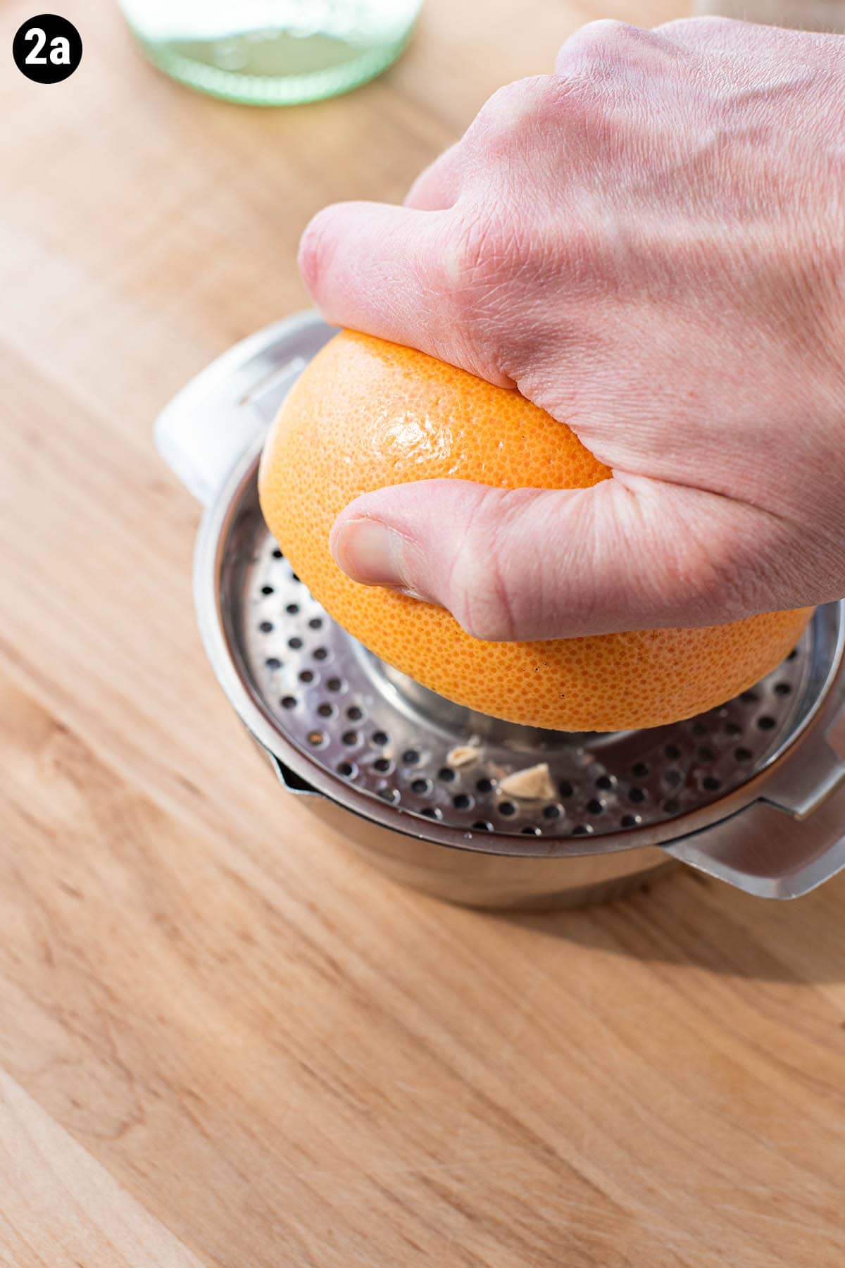 A hand juicing half a grapefruit slice with a stainless citrus juicer.