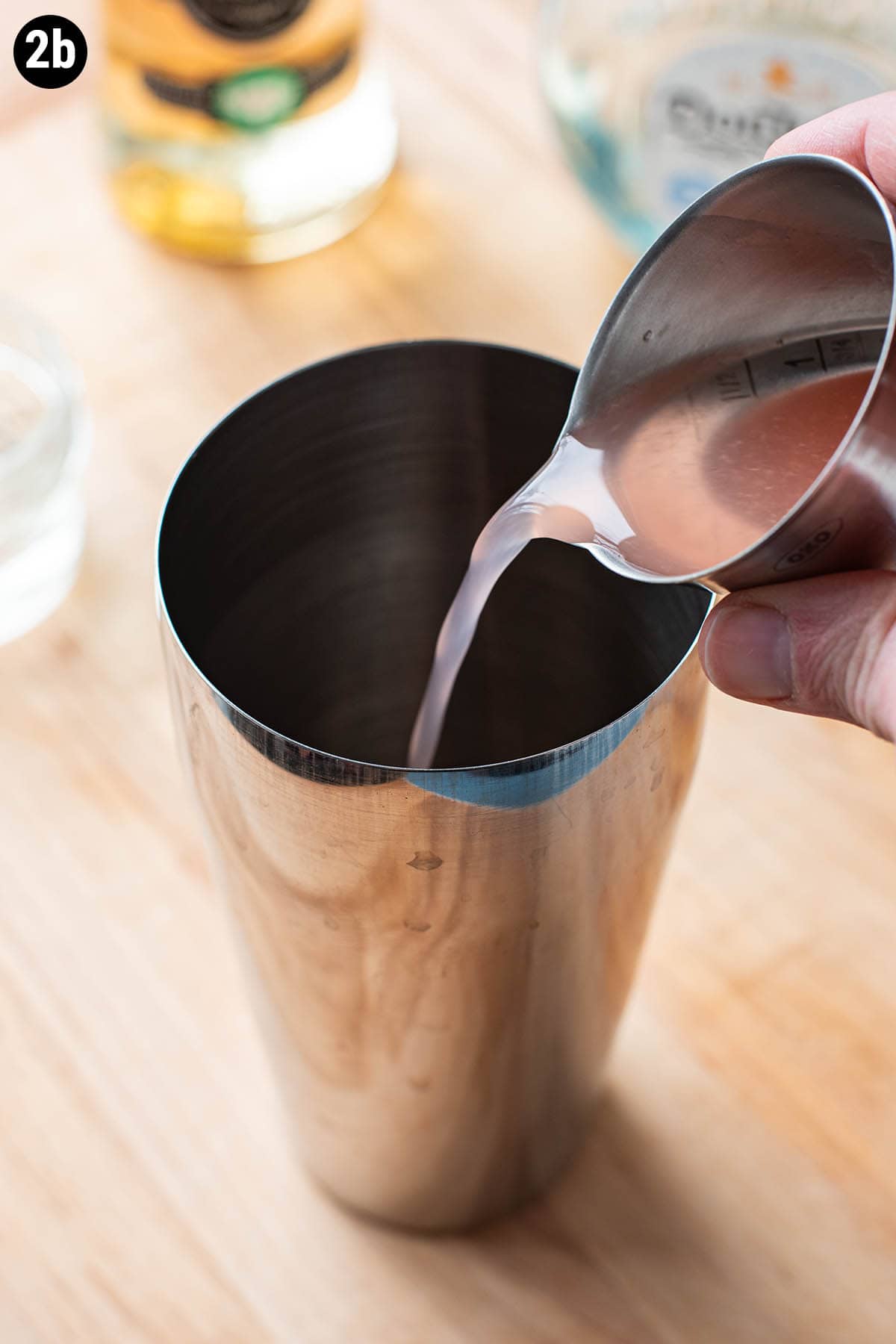 Pouring an ounce of fresh grapefruit juice into a cocktail shaker with a double jigger.