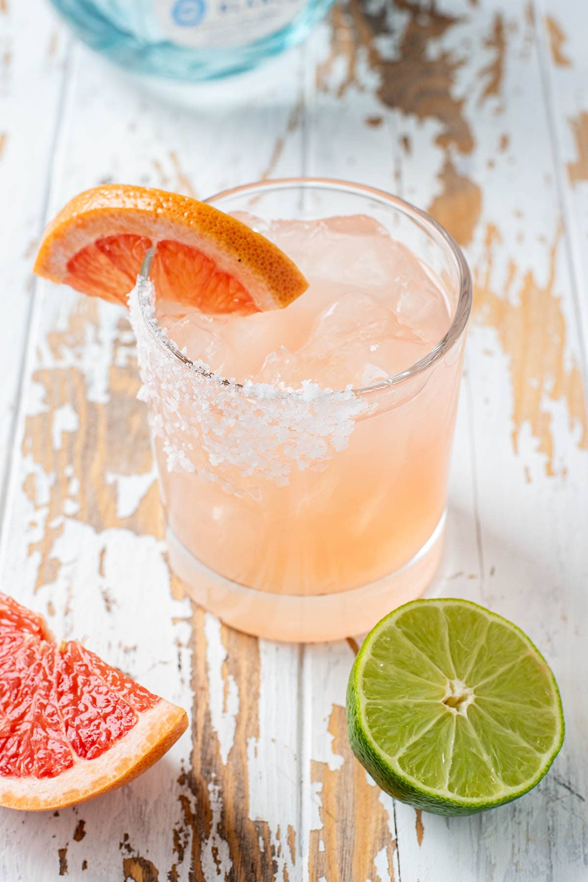 A pink hued grapefruit margarita served with a grapefruit wedge and salted rim.