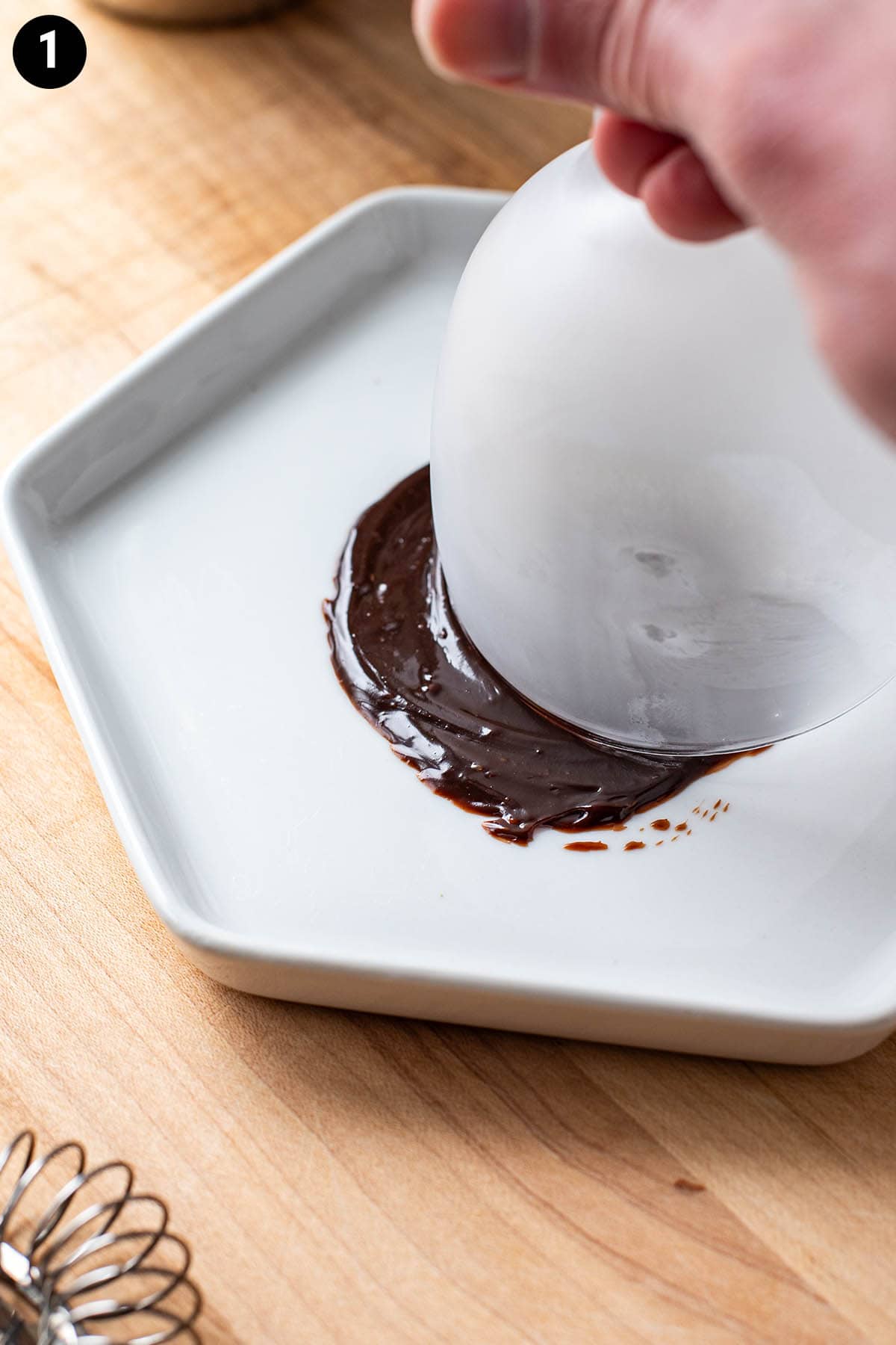 Adding a rim of chocolate to a frozen Nick and Nora glass by dipping it in melted chocolate.