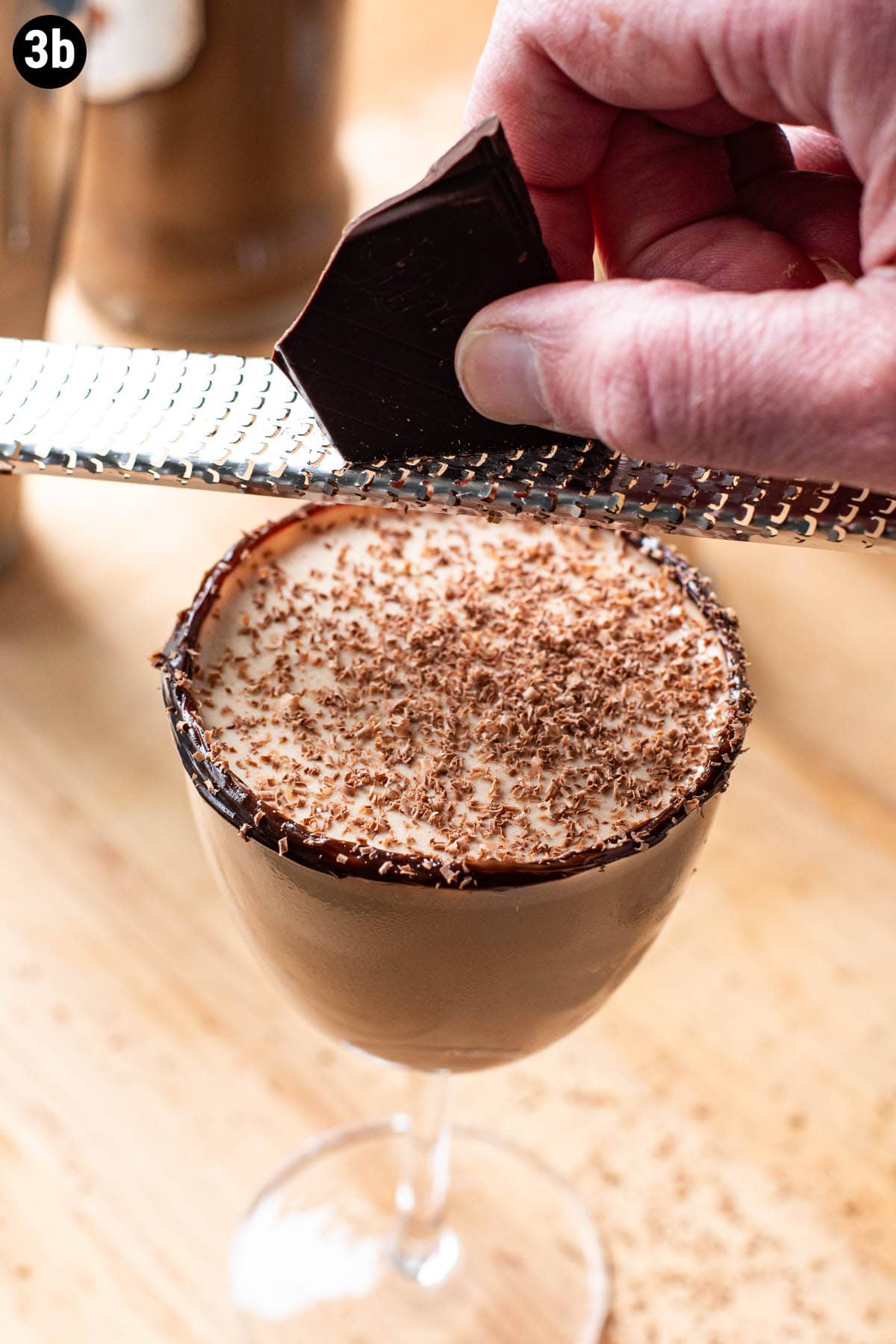 A hand grating a chunk of chocolate over the top of a chocolate martini.