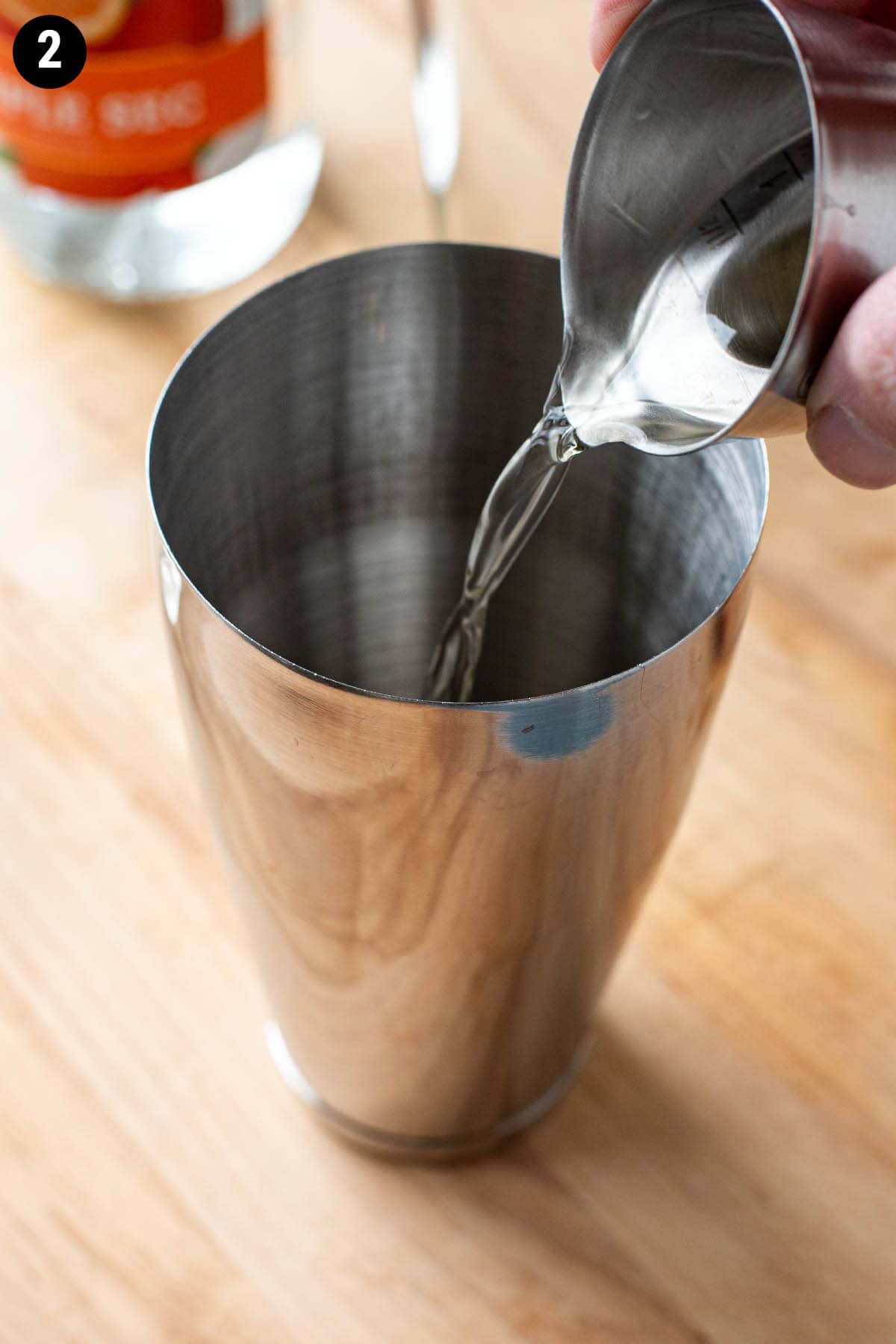A hand pouring a double jigger of vodka into a cocktail shaker.