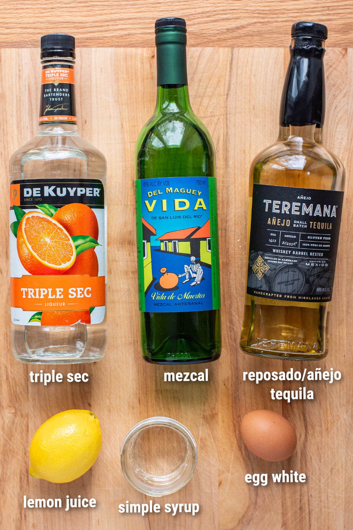 Tequila and mezcal sour cocktail ingredients laid out on a wooden cutting board.