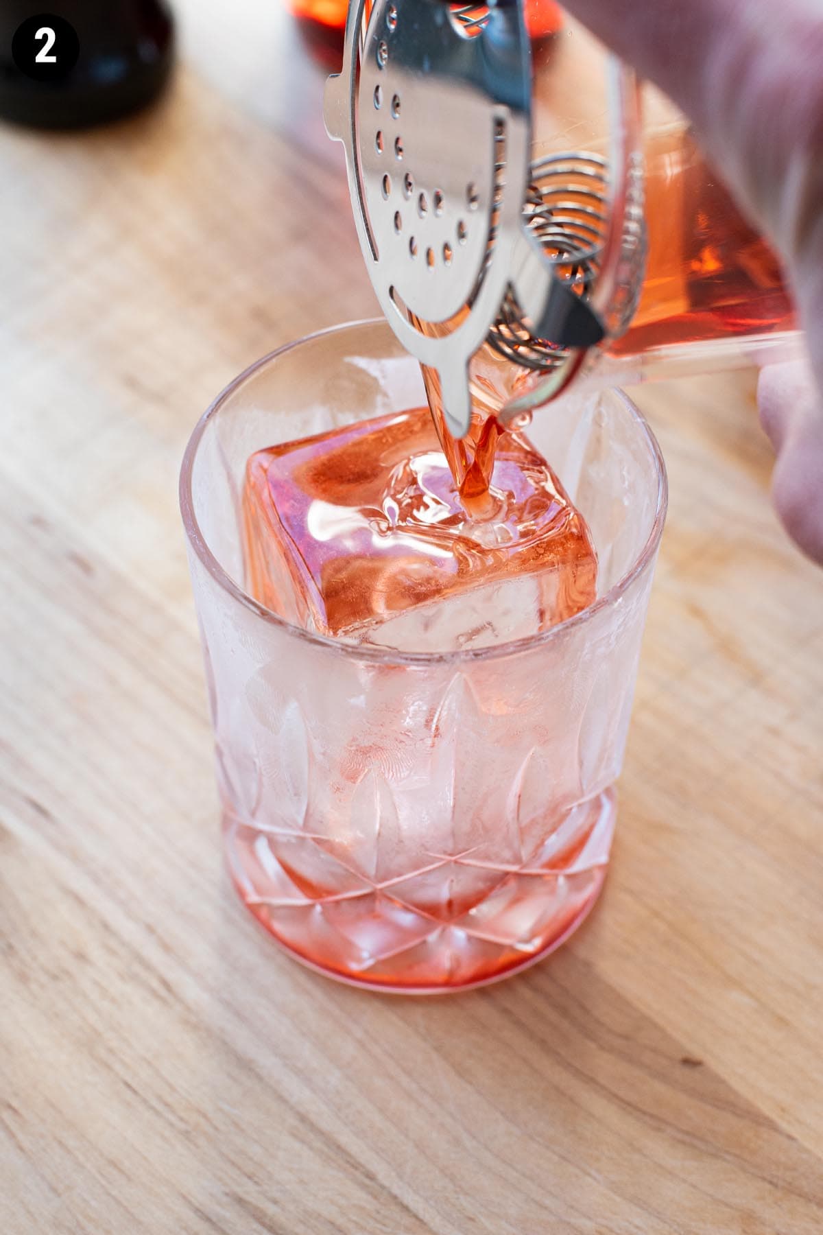 Straining a Boulevardier cocktail into a chilled glass over a giant clear ice cube.
