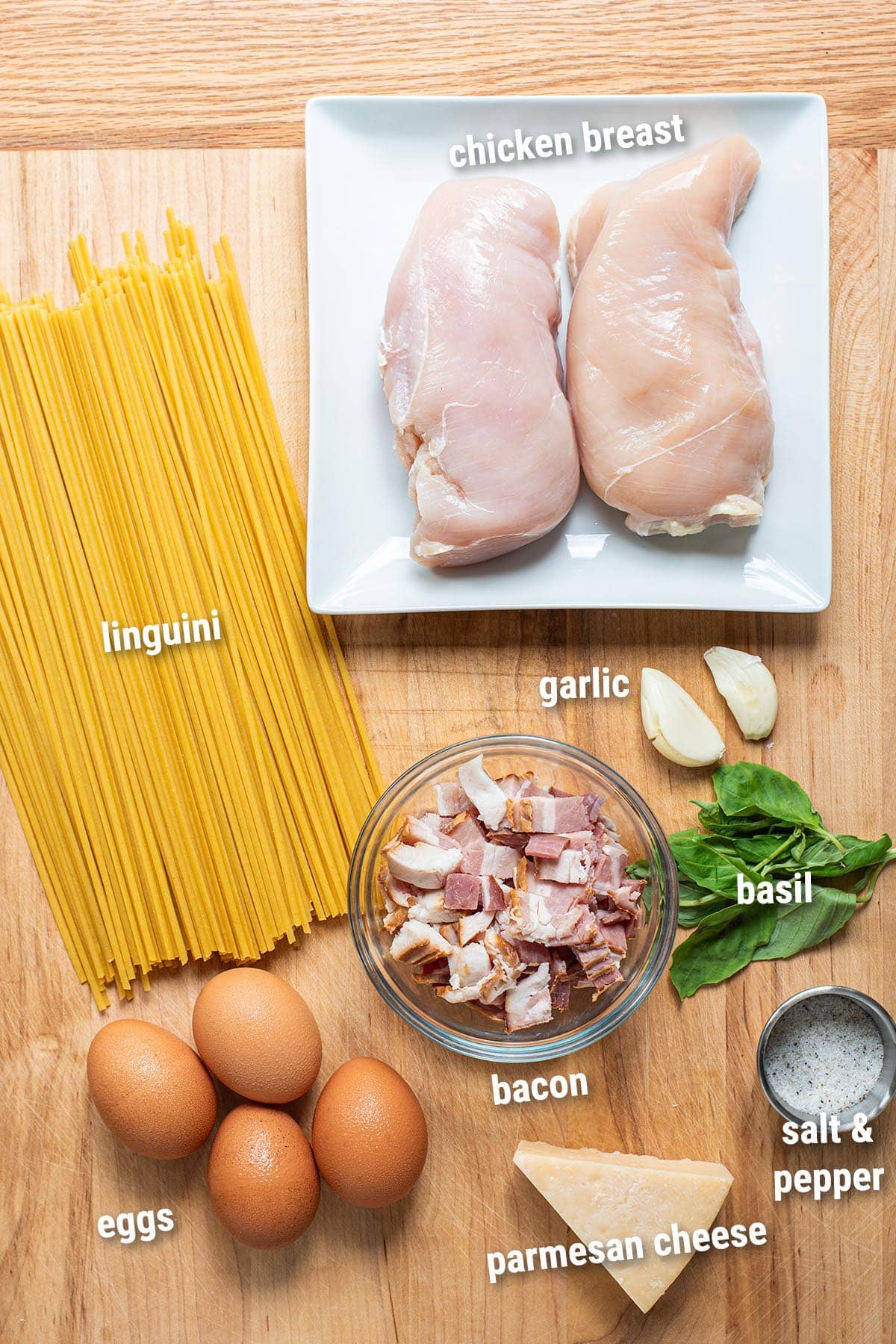 Raw, uncooked chicken carbonara ingredients laid out on a wooden cutting board.