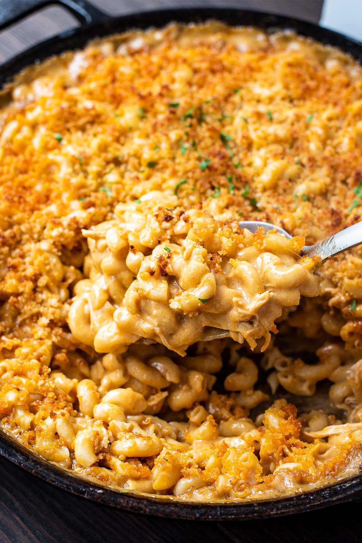 Close up golden baked buffalo chicken mac and cheese in a cast iron skillet with a large spoonful lifting away.