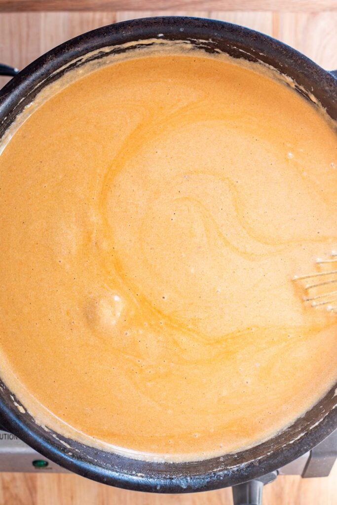 A creamy orange buffalo and cheese sauce cooking in a cast iron skillet.