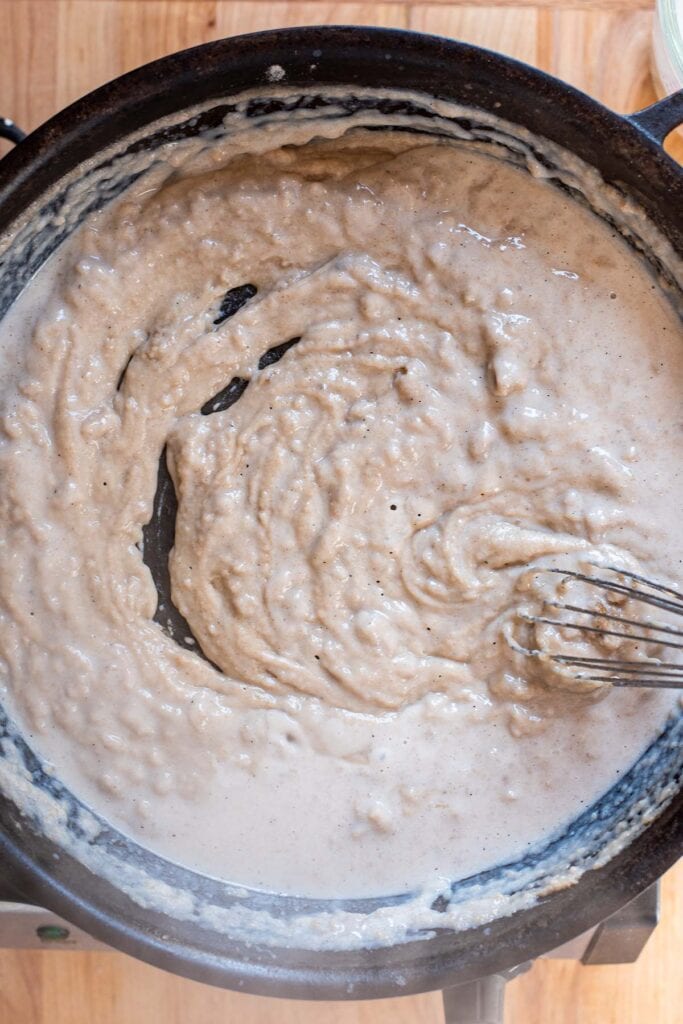 A lumpy roux forming with milk in a cast iron skillet.