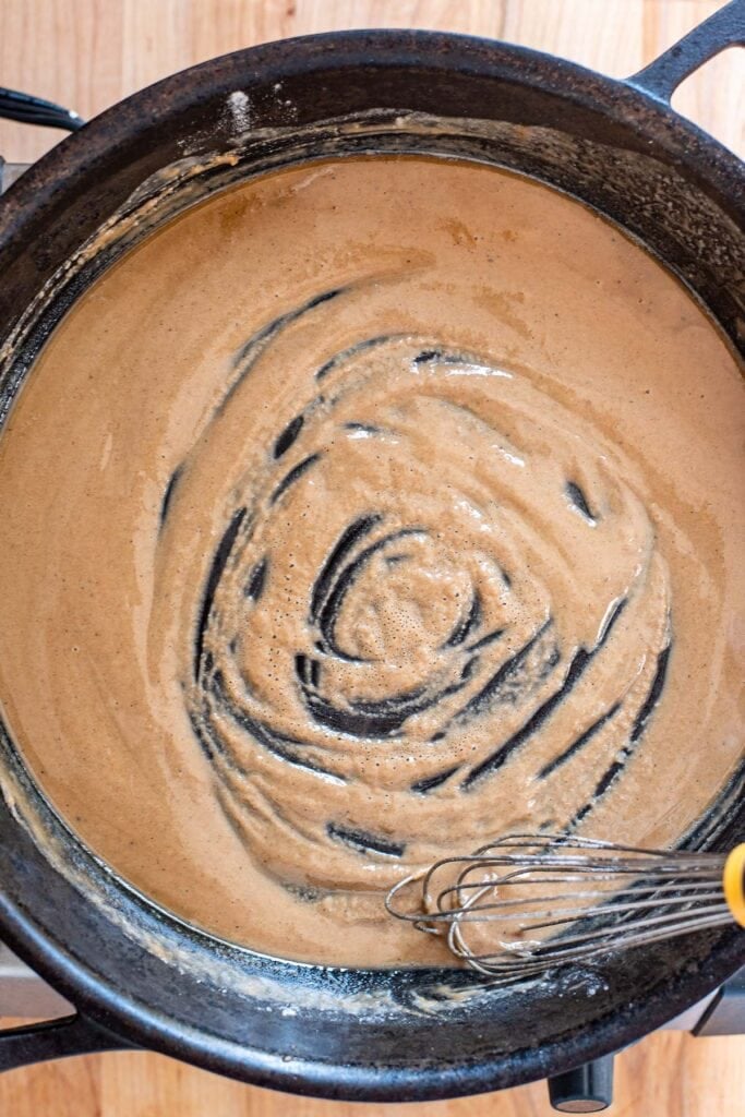 Stirring a golden roux with a whisk in a cast iron skillet.