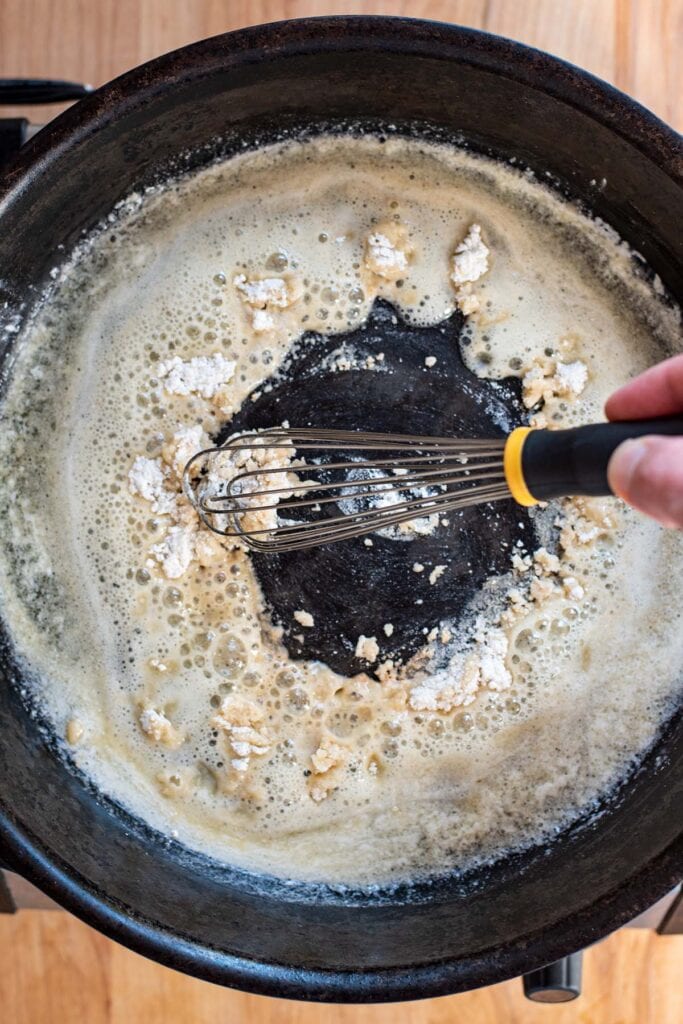 Whisking flour into melted butter in a cast iron skillet.