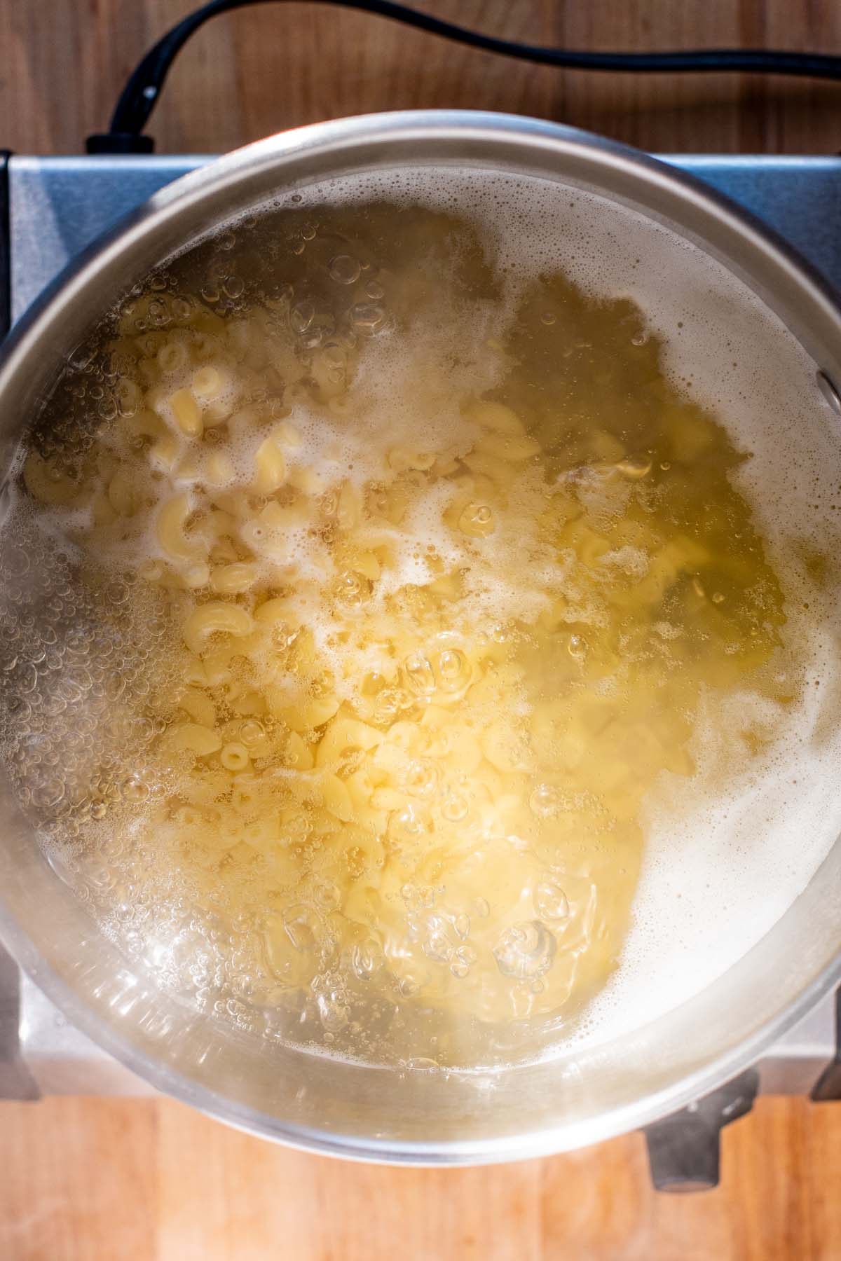 Overhead view of elbow macaroni noodles boiling in a large pot of water.
