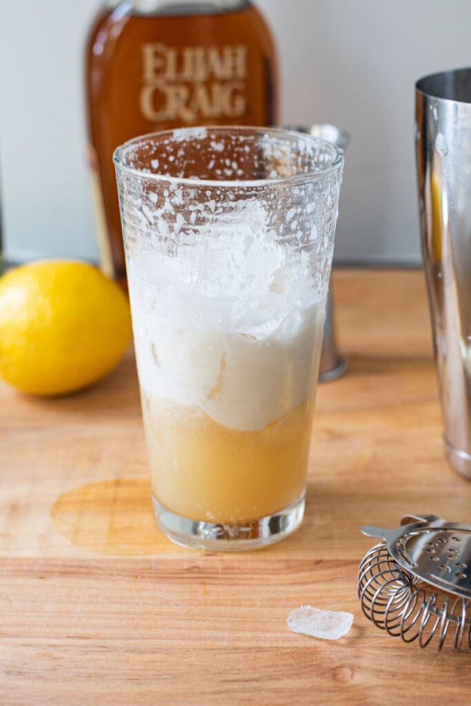 A cocktail shaker with frothed egg white and ice added.