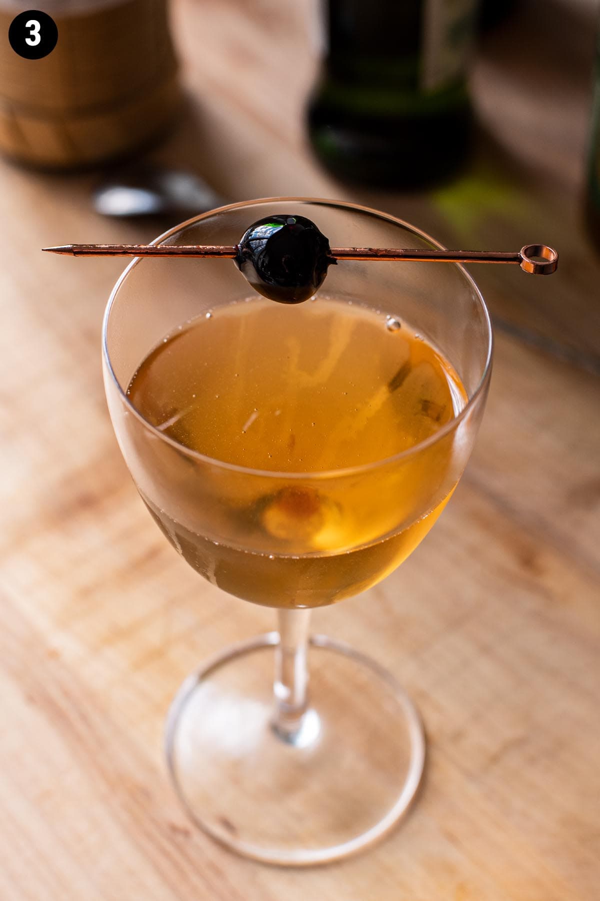 A Brooklyn cocktail in a Nick and Nora glass garnished with a Luxardo cherry.