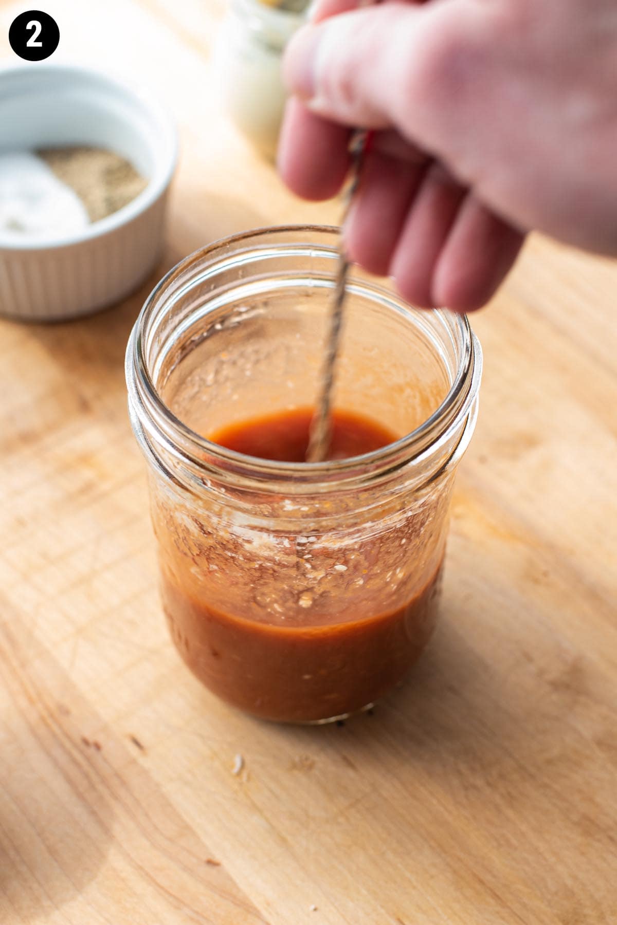 Stirring homemade Bloody Mary mix in a glass jar with a bar spoon.