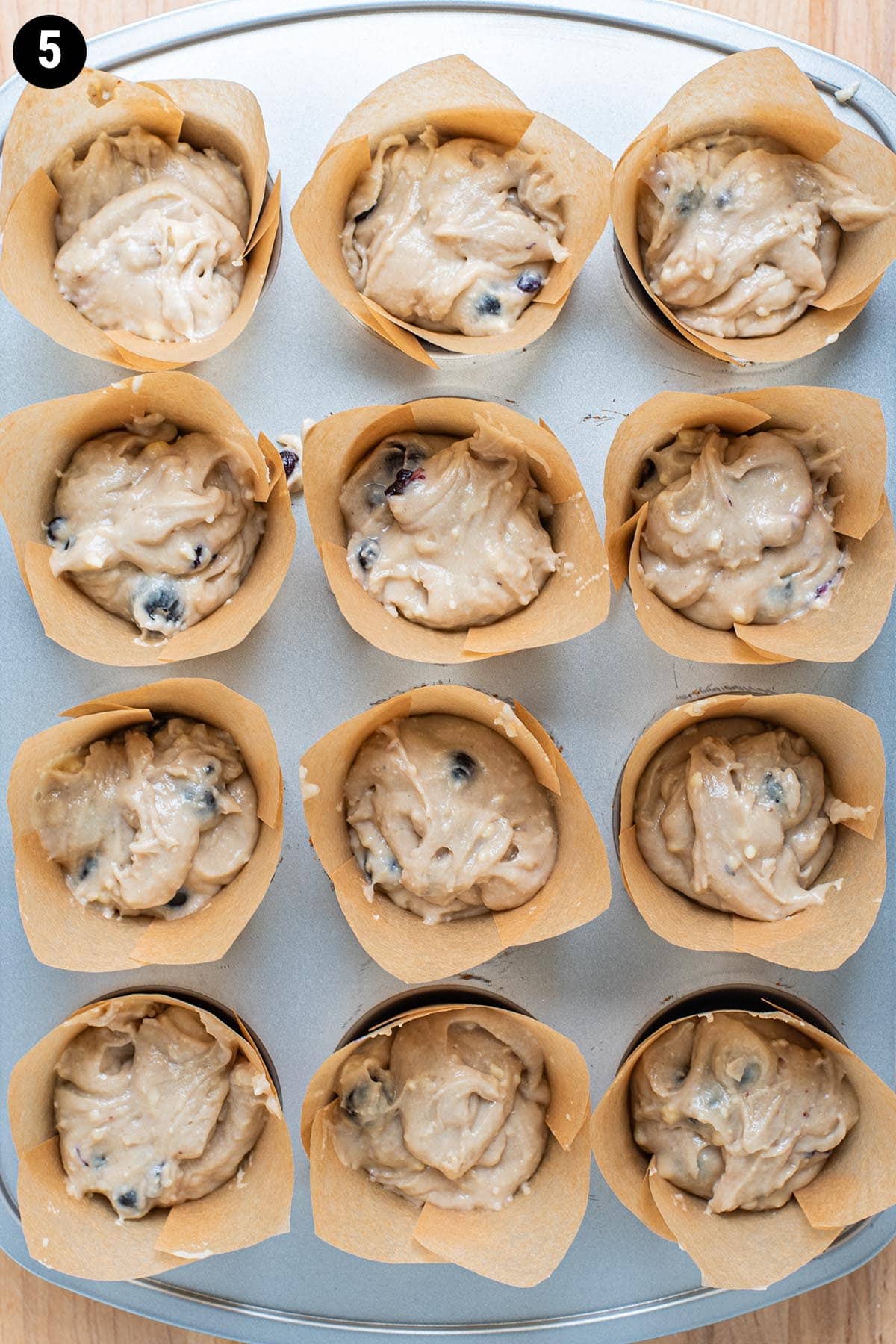 Raw, uncooked muffin batter in a muffin run lines with brown muffin liners.