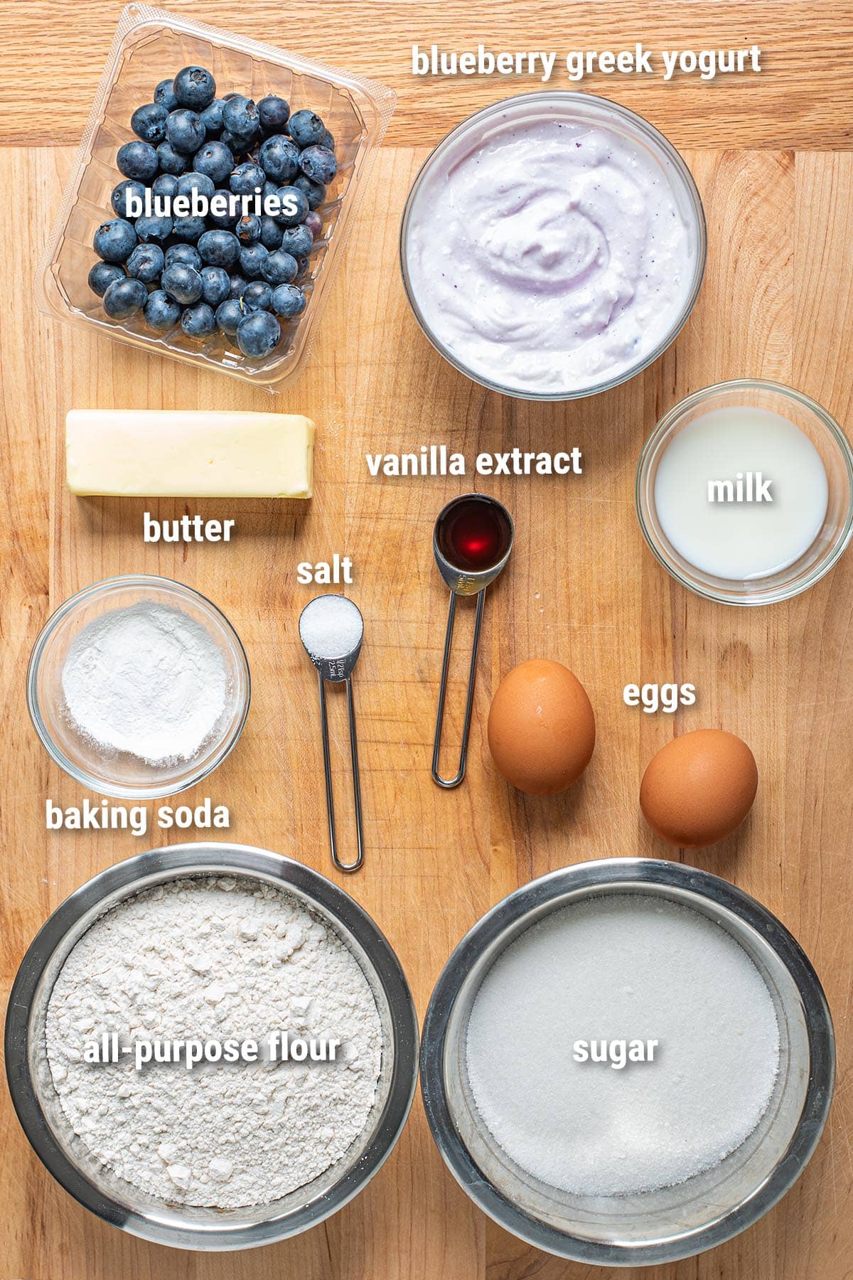 Raw, uncooked blueberry muffin ingredients laid out on a wooden cutting board.
