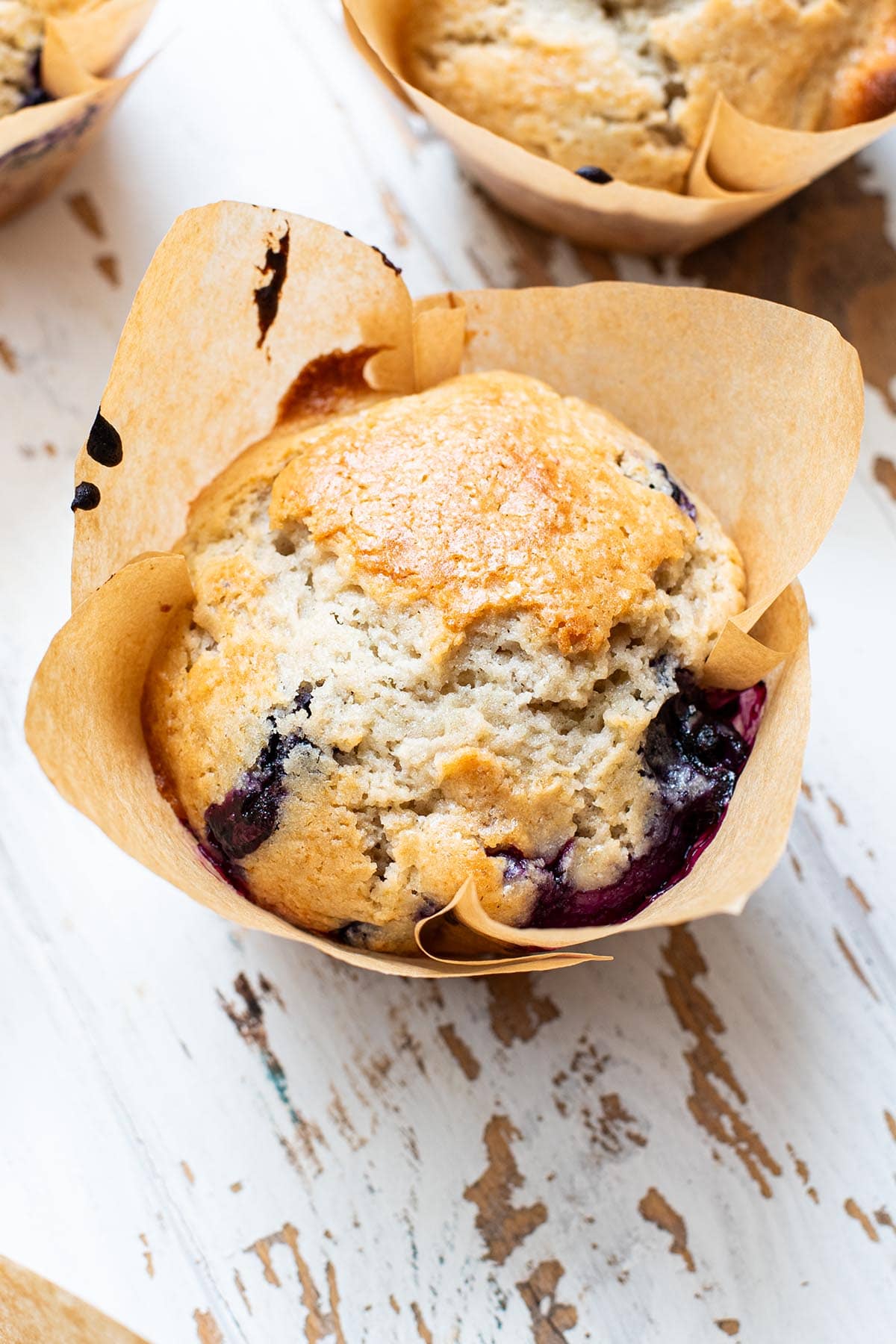 A golden baked blueberry muffin made with Greek yogurt on a white rustic wooden table.