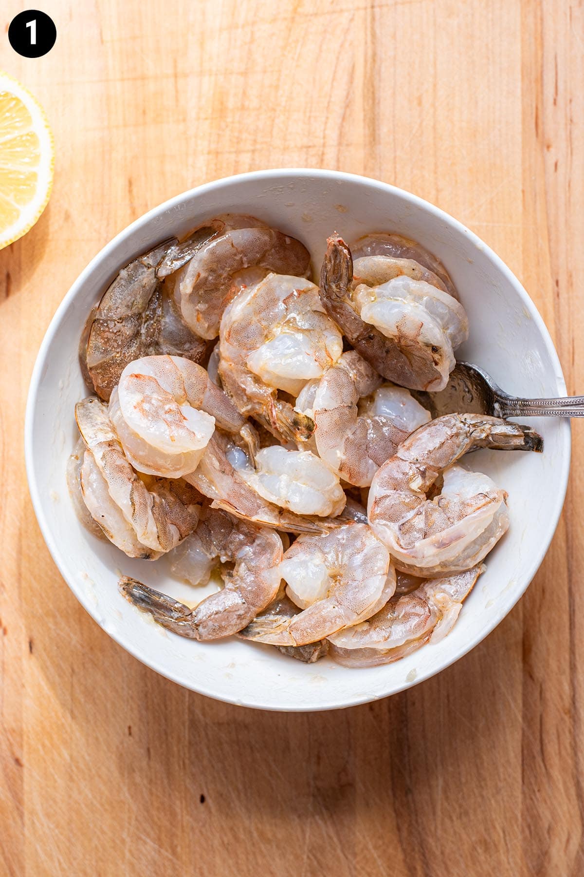 Raw, uncooked shrimp in a small white bowl.