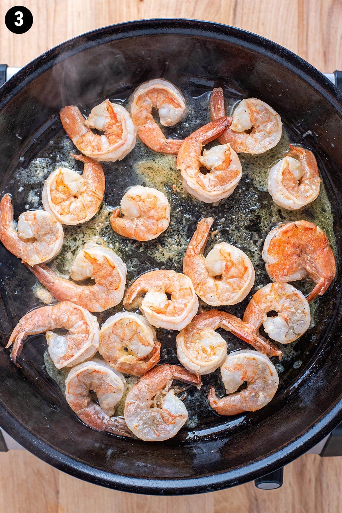 Shrimp cooking in a cast iron skillet with garlic, olive oil, and lemon juice.