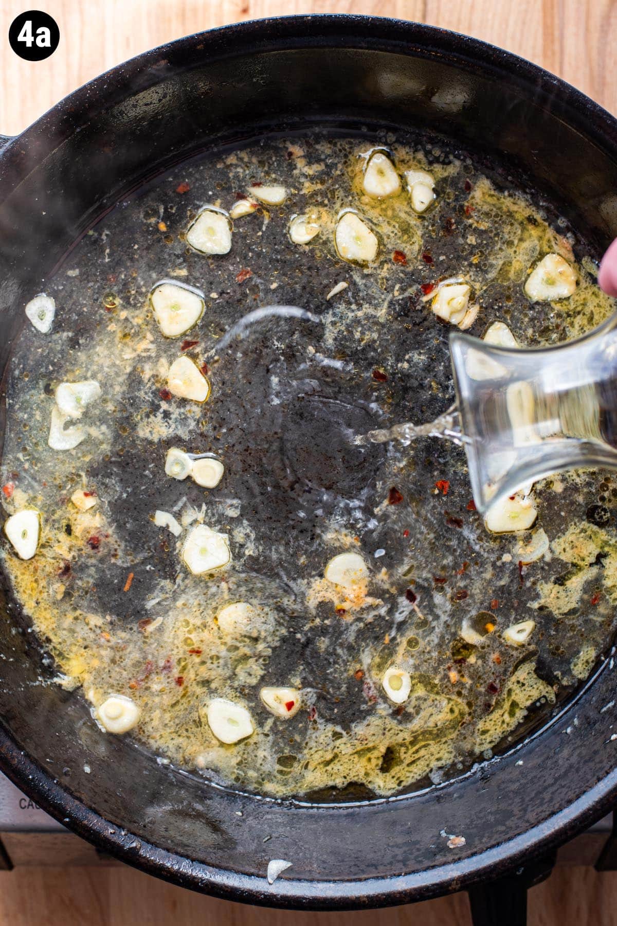 Pouring white wine into a skillet with sliced garlic and butter.